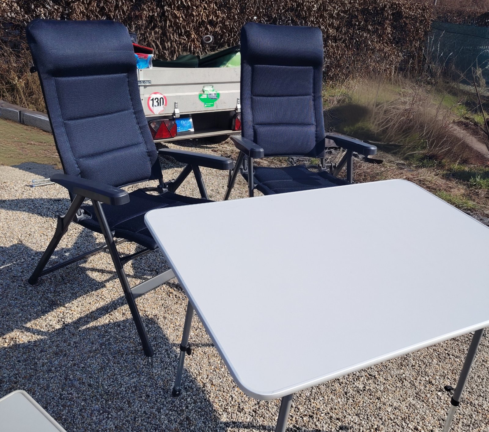 Na obrázku jsou dvě skládací židle a stolek u karavanu. Ideální pro venkovní posezení a relaxaci.
