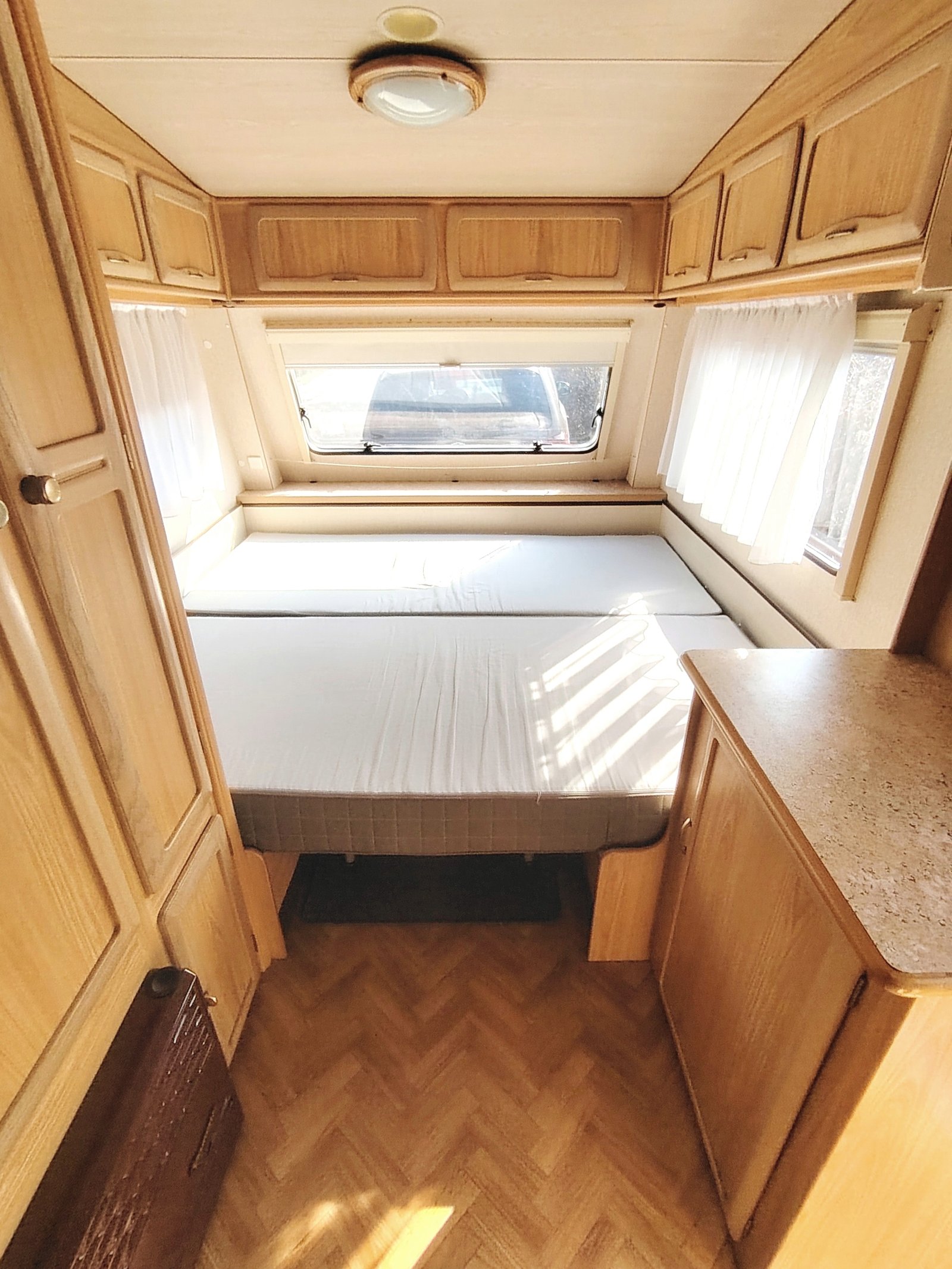 Prostorný karavan s dřevěným interiérem, komfortní dvoulůžko, úložné skříňky a střešní okno. Ideal pro dovolenou.