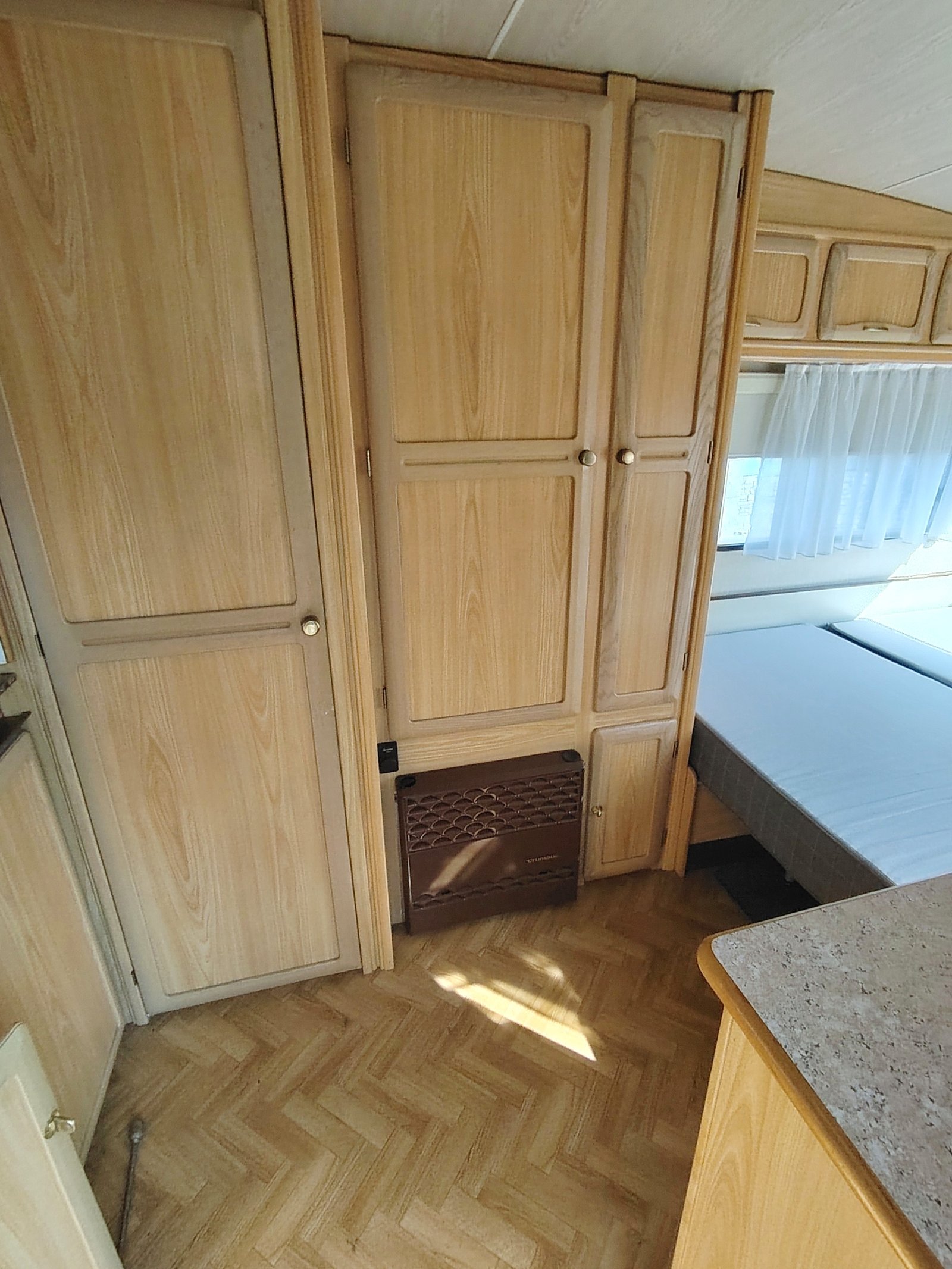 Interiér karavanu s dřevěnými skříněmi a manželskou postelí. Ideální pro pohodlné cestování.