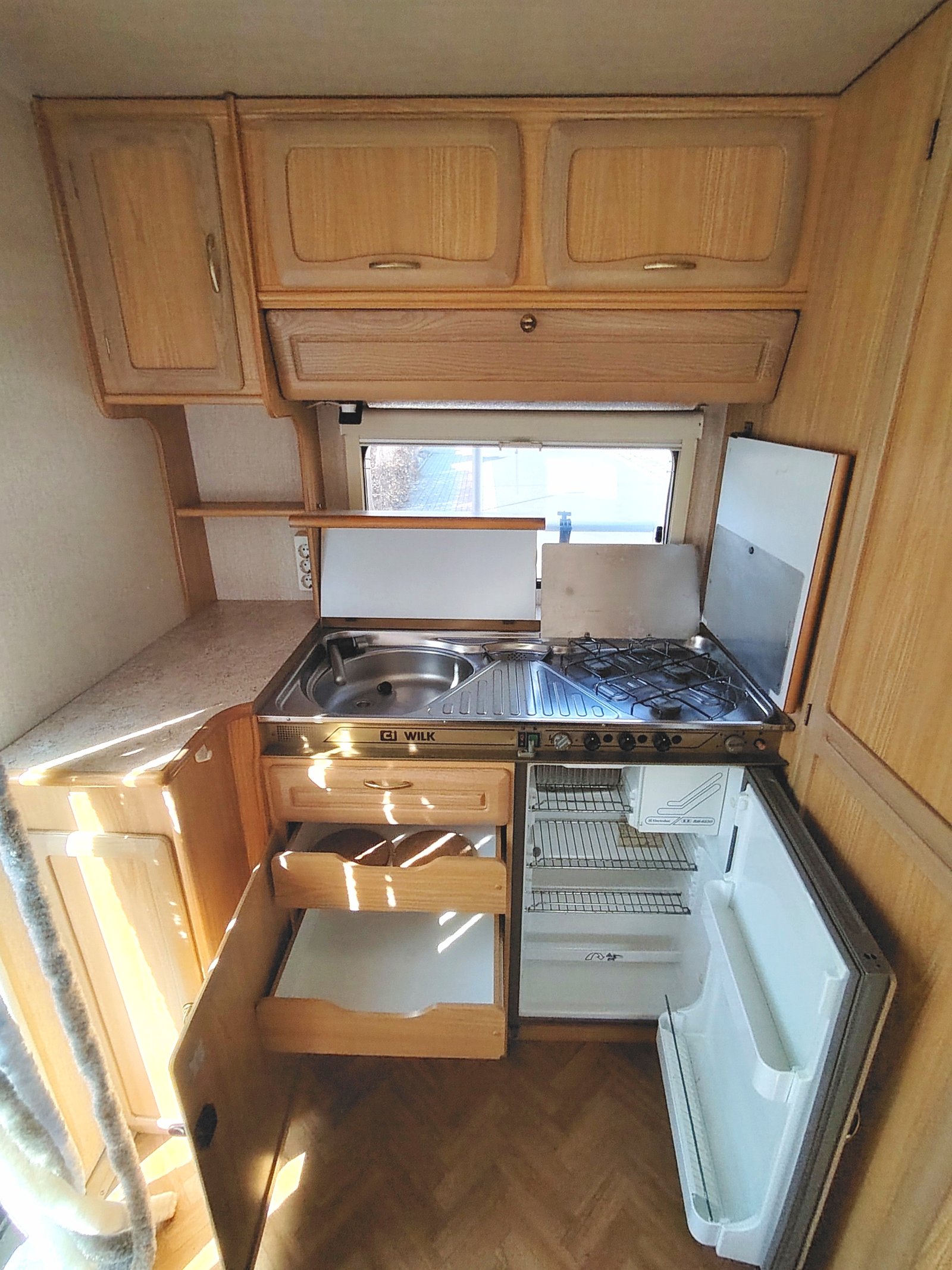 Kuchyňka v karavanu Wilk, vybavená dřezem, sporákem a lednicí, ideální pro cestování a kempování.