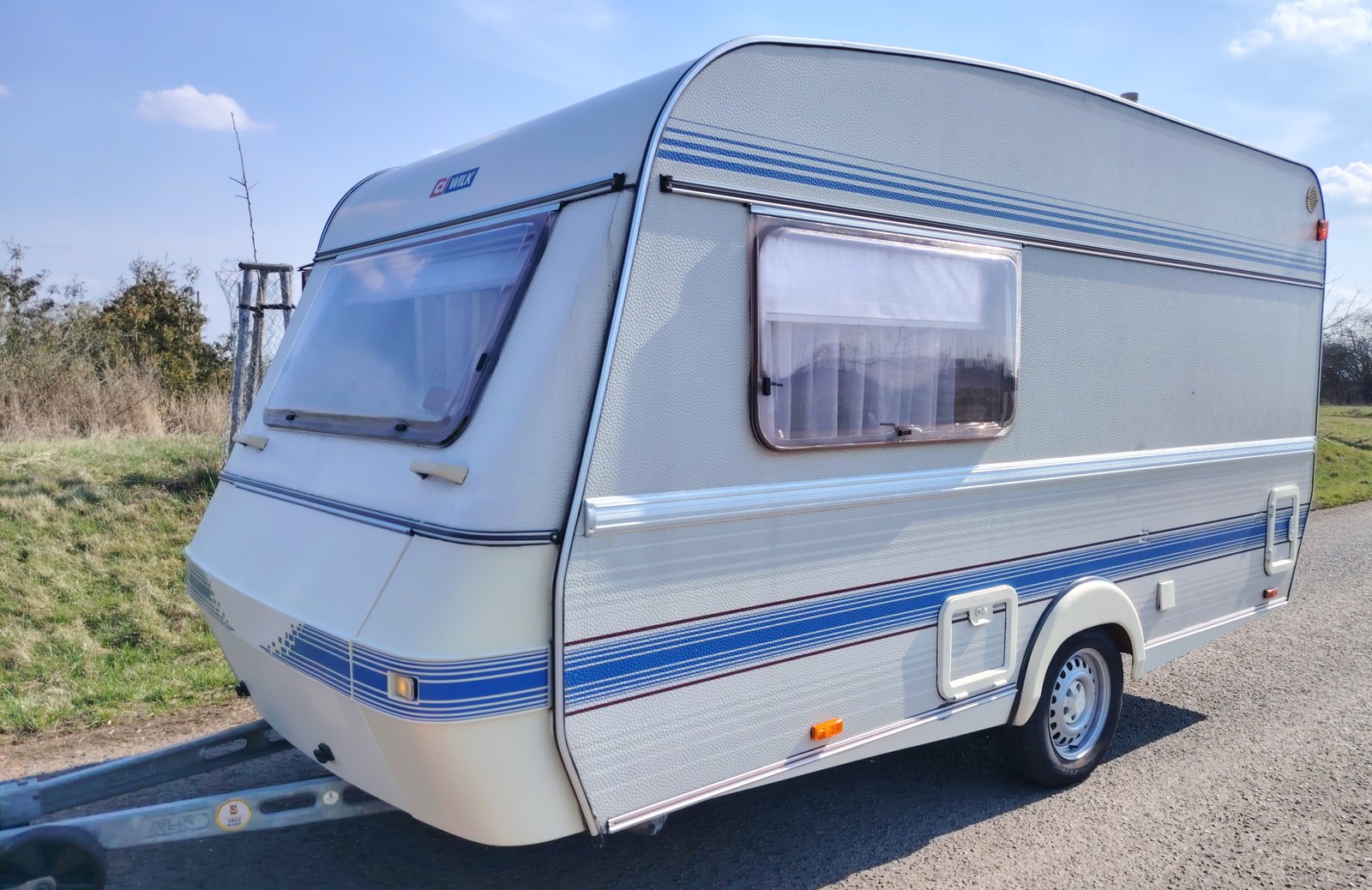 Karavan s modro-bílými pruhy, vhodný pro pohodlné cestování a rekreaci v přírodě.