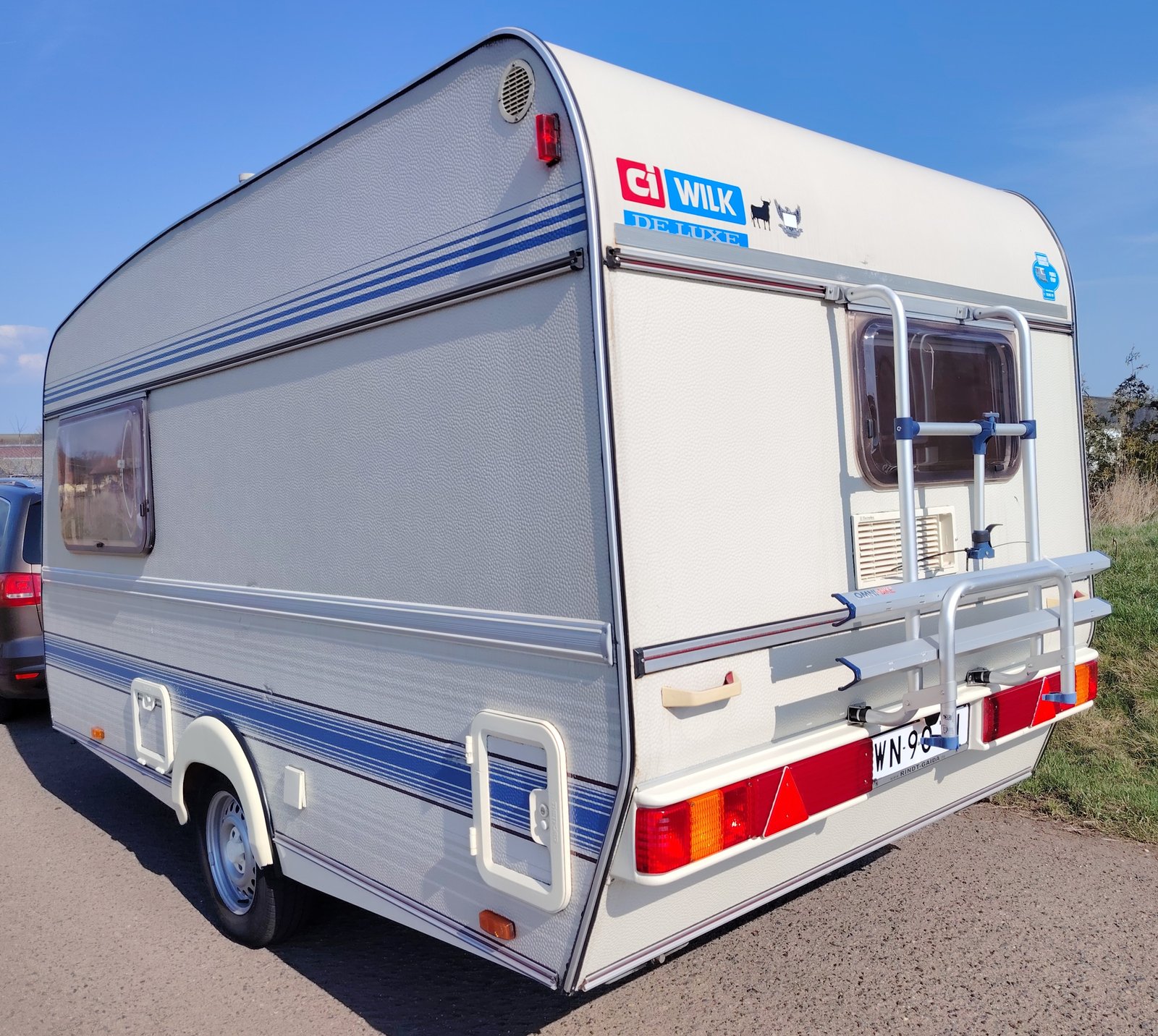 Karavan CI Wilk Deluxe s modro-bílými pruhy, ideální pro pohodlné cestování a kempování.