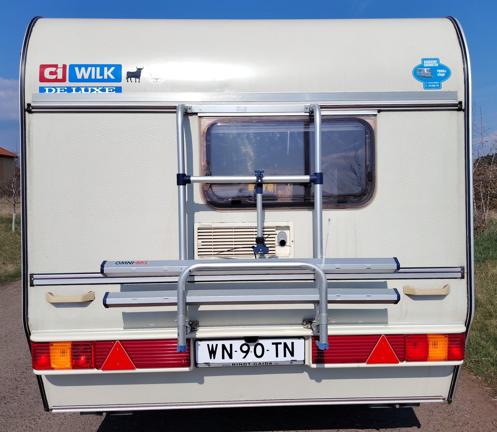 Karavan CI Wilk De Luxe s připevněným držákem na kolo, ideální pro pohodlné cestování a kempování.