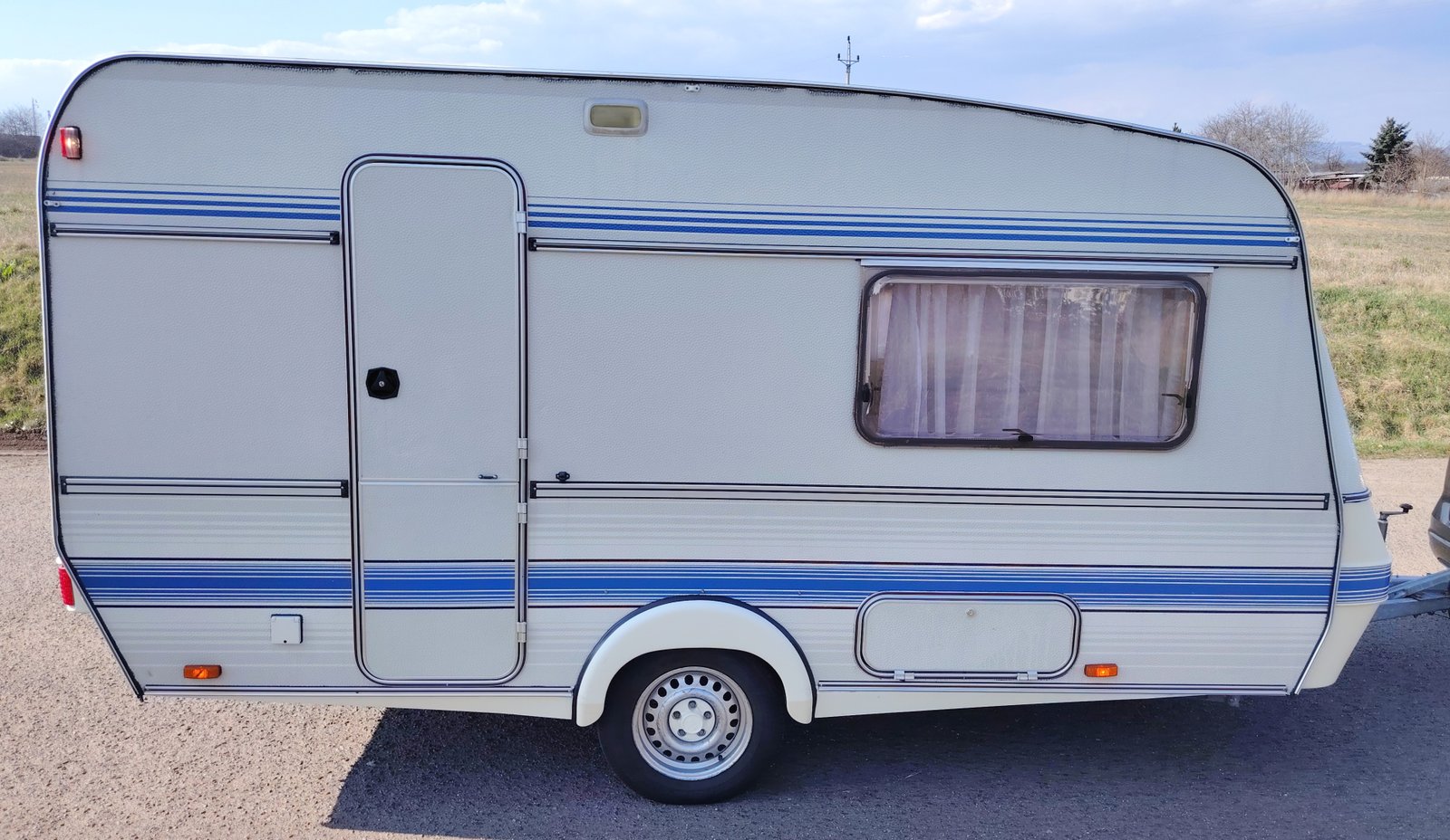 Bílý karavan se modrými pruhy, ideální pro kempování a cestování.