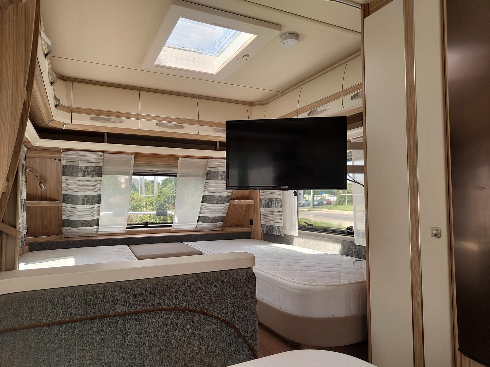 Obrázek interiéru karavanu s moderním designem, pohodlnými lůžky a televizí. Ideální pro příjemné cestování.