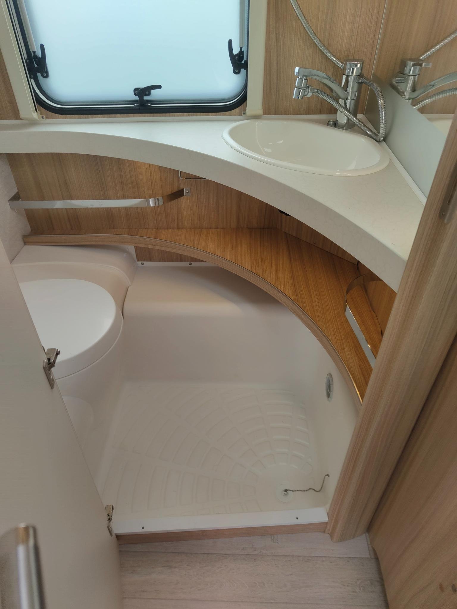 Interiér karavanu s moderním umyvadlem a sprchovým koutem. Elegantní dřevěné detaily pro pohodlí.