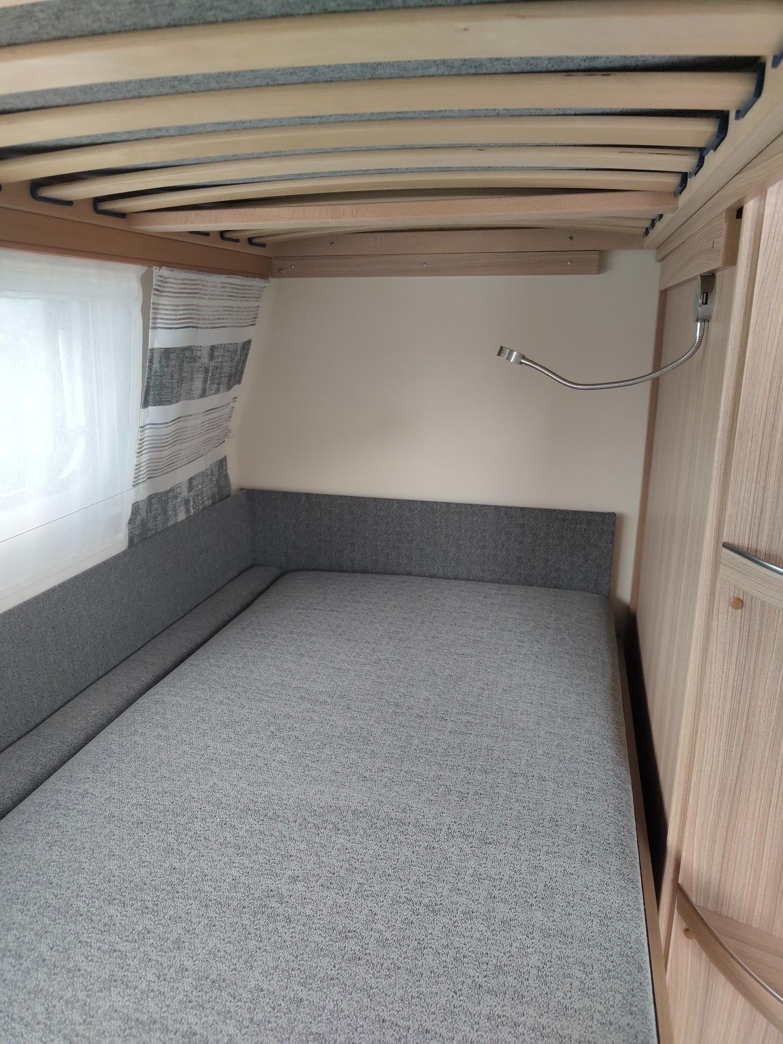 Obrázek ukazuje interiér karavanu s pohodlnou šedou sedačkou a moskytiérou u okna.