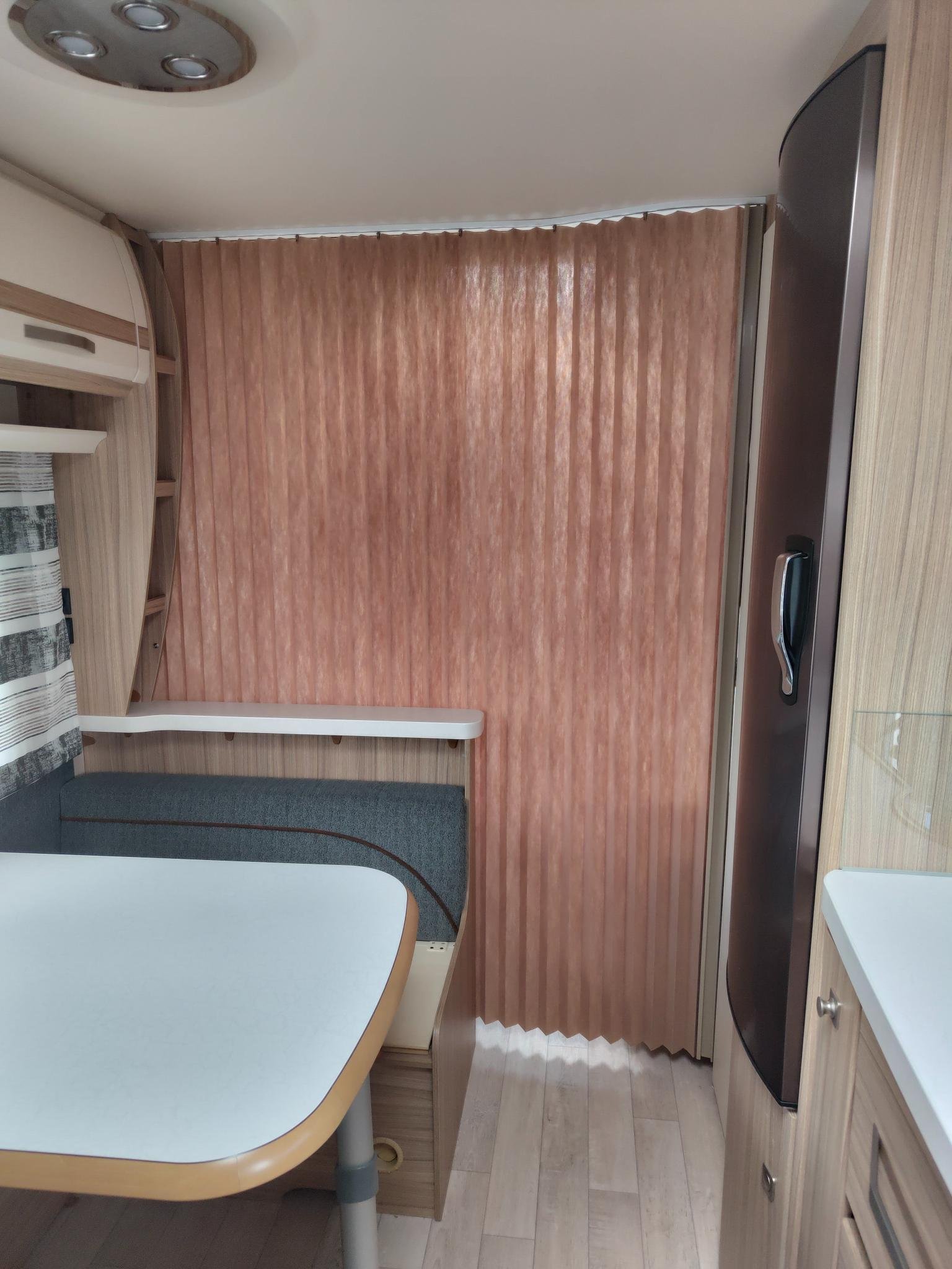 Interiér moderního karavanu s pohodlným posezením a chladničkou. Vkusné dřevo a příjemné osvětlení.