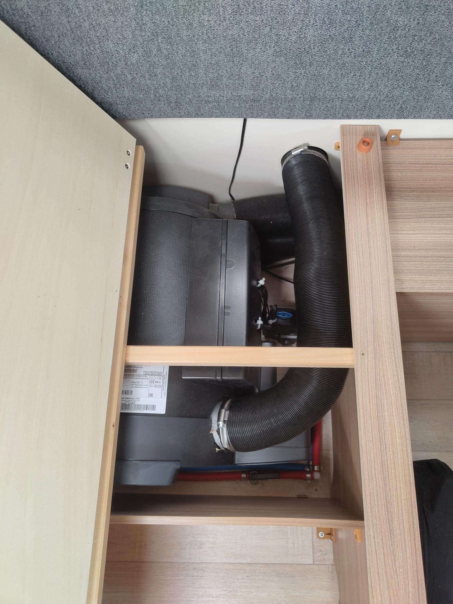 Obrázek zobrazuje část interiéru obytného auta s motorem a připojenými hadicemi, připravený na cestování.