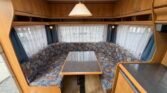 Interiér karavanu s pohodlným sezením a stolem, ideální pro rodinné výlety. Značka a model nejsou viditelné.