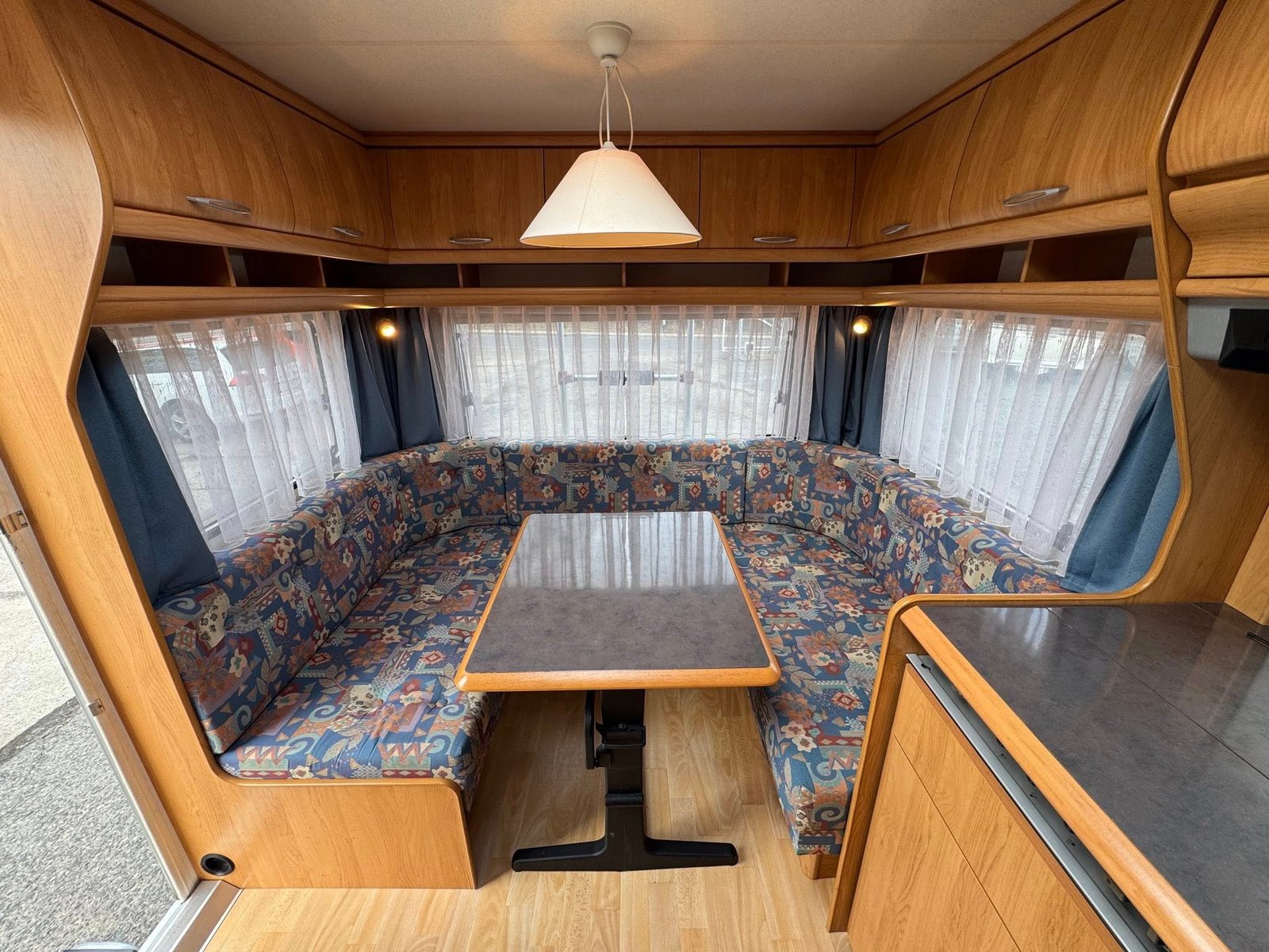 Interiér karavanu s pohodlným sezením a stolem, ideální pro rodinné výlety. Značka a model nejsou viditelné.
