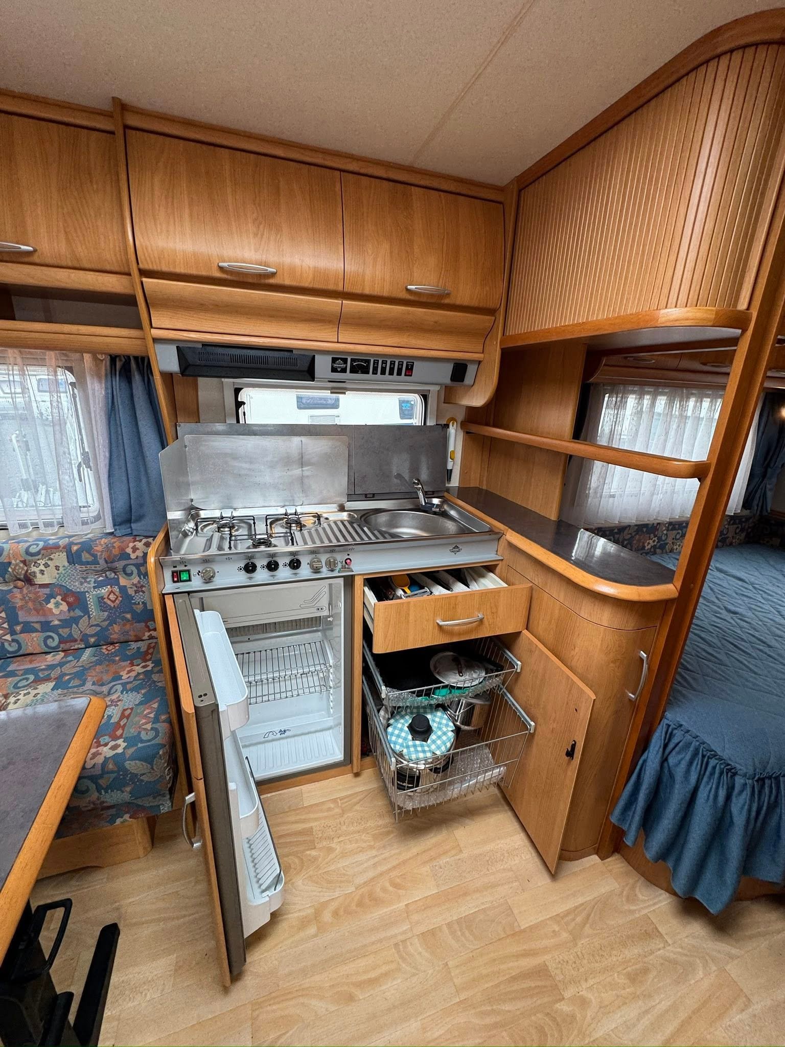 Obrázek interiéru karavanu s kuchyňským koutem, lednicí a úložnými prostory pro pohodlné cestování.