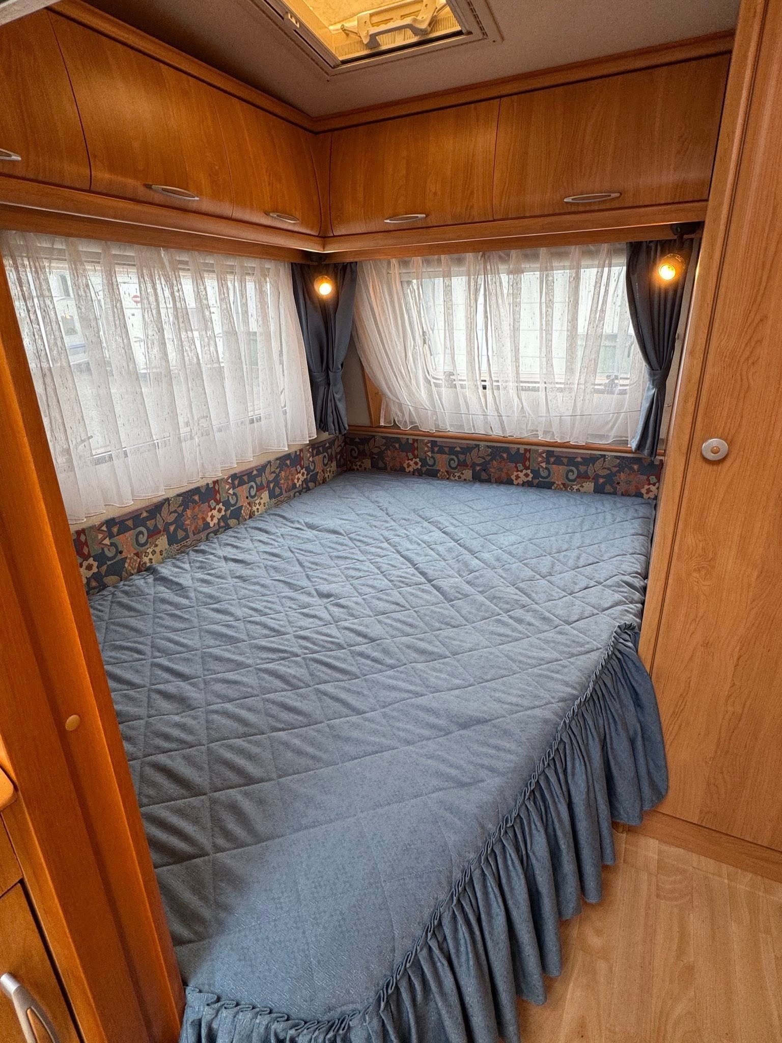 Stylový karavan s prostornou postelí a dřevěným interiérem. Ideální pro pohodlné cestování.