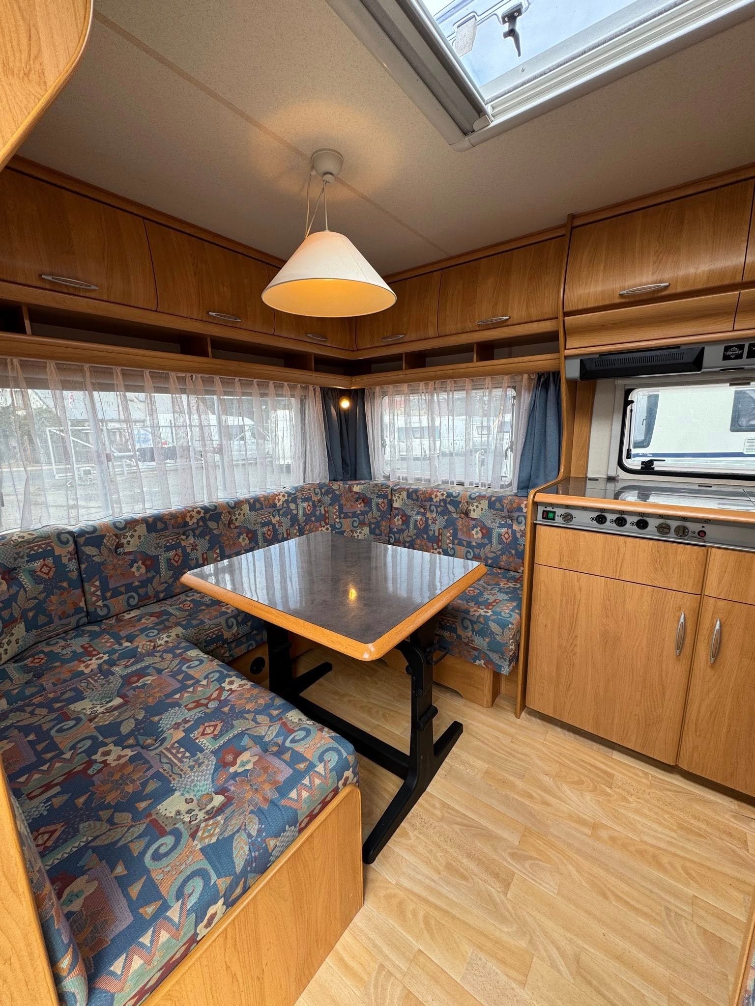 Obrázek interiéru karavanu s pohodlným posezením a kuchyňským koutem, ideální pro cestování a odpočinek.