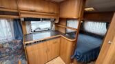 Interiér karavanu s kuchyňkou a ložnicí, útulný design a dostatek úložného prostoru. Ideální pro dovolenou.