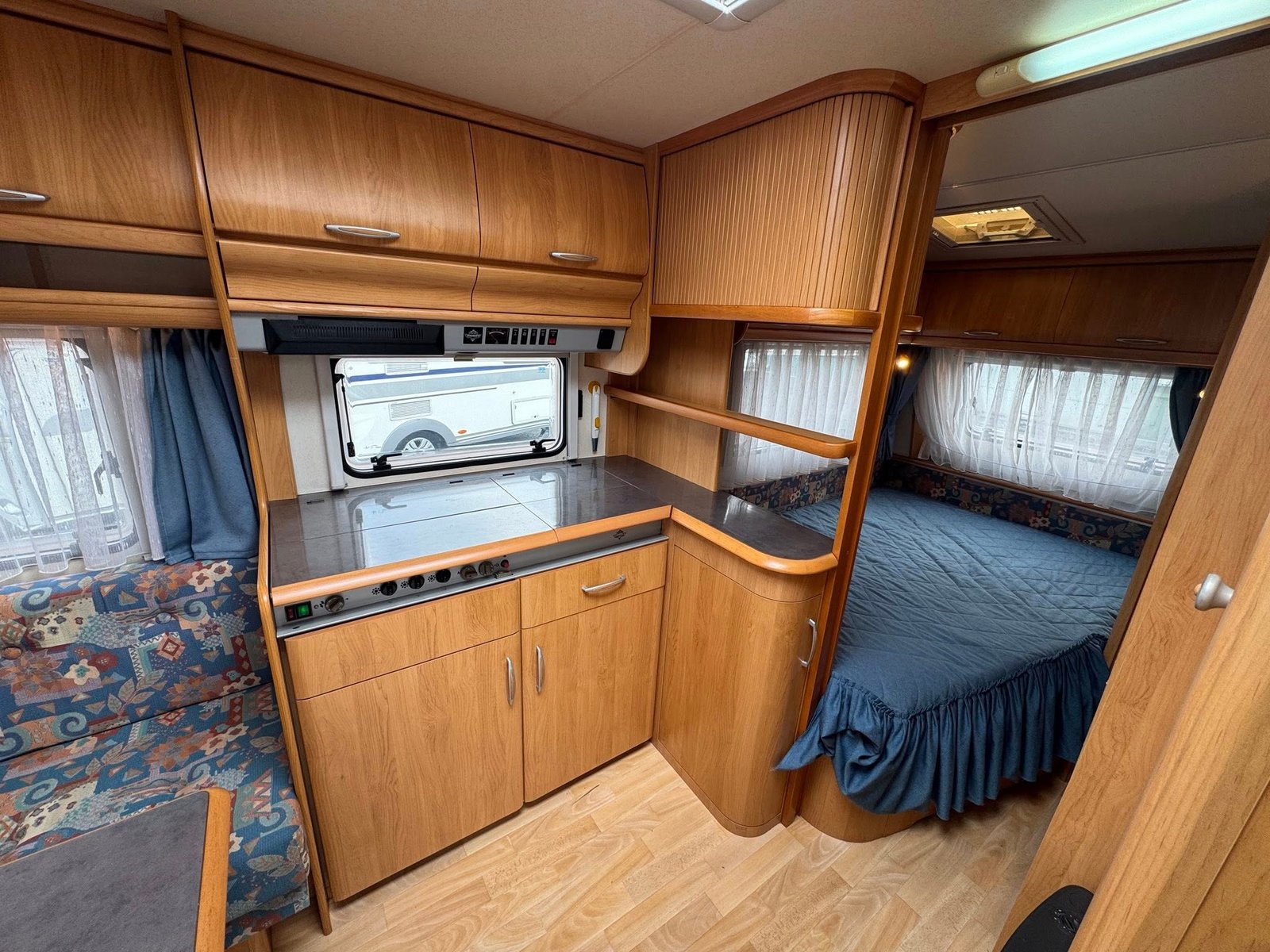 Interiér karavanu s kuchyňkou a ložnicí, útulný design a dostatek úložného prostoru. Ideální pro dovolenou.