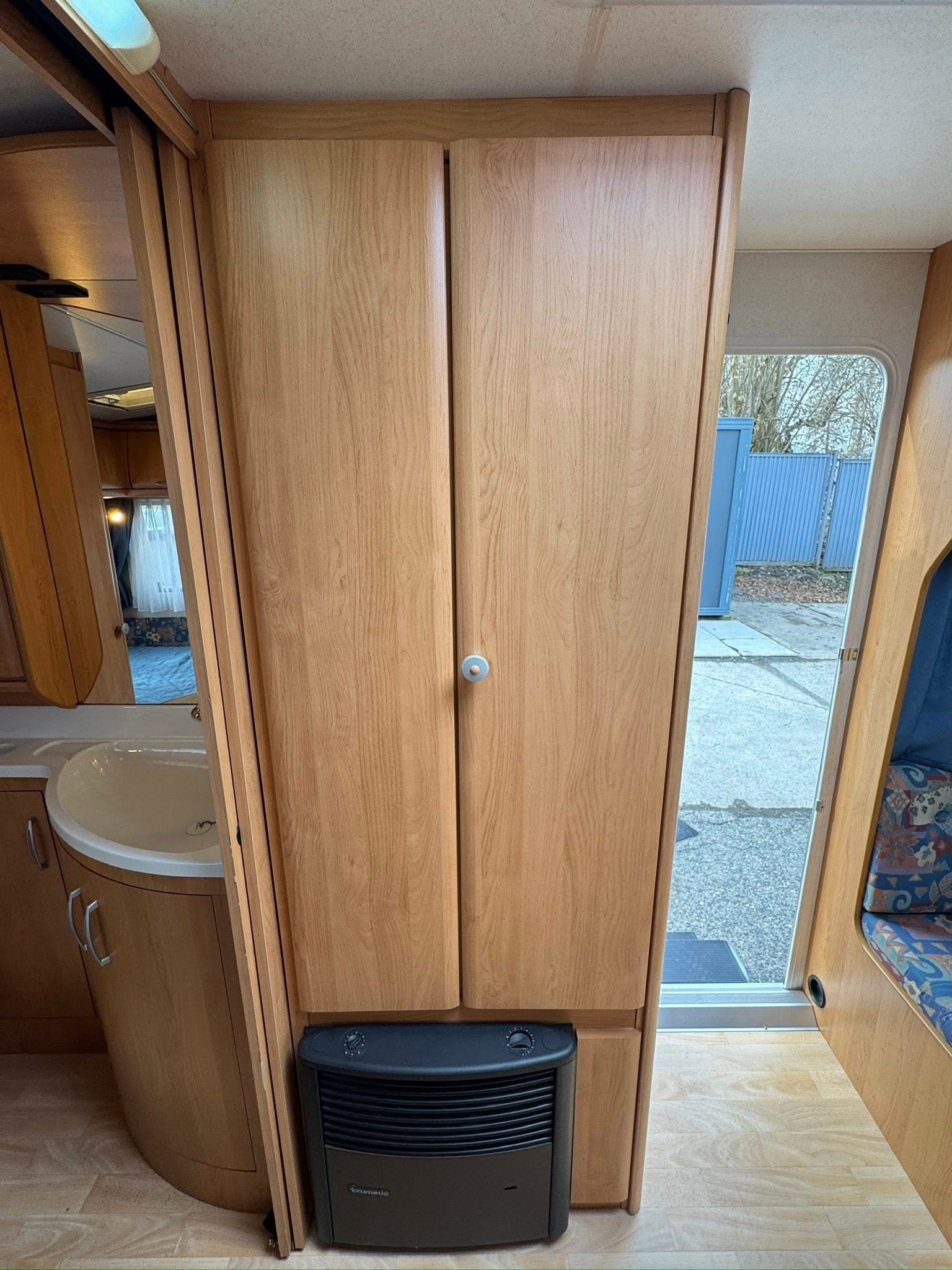 Obrázek interiéru karavanu, s dřevěnými skříněmi a umyvadlem, vytváří příjemnou atmosféru pro cestování.