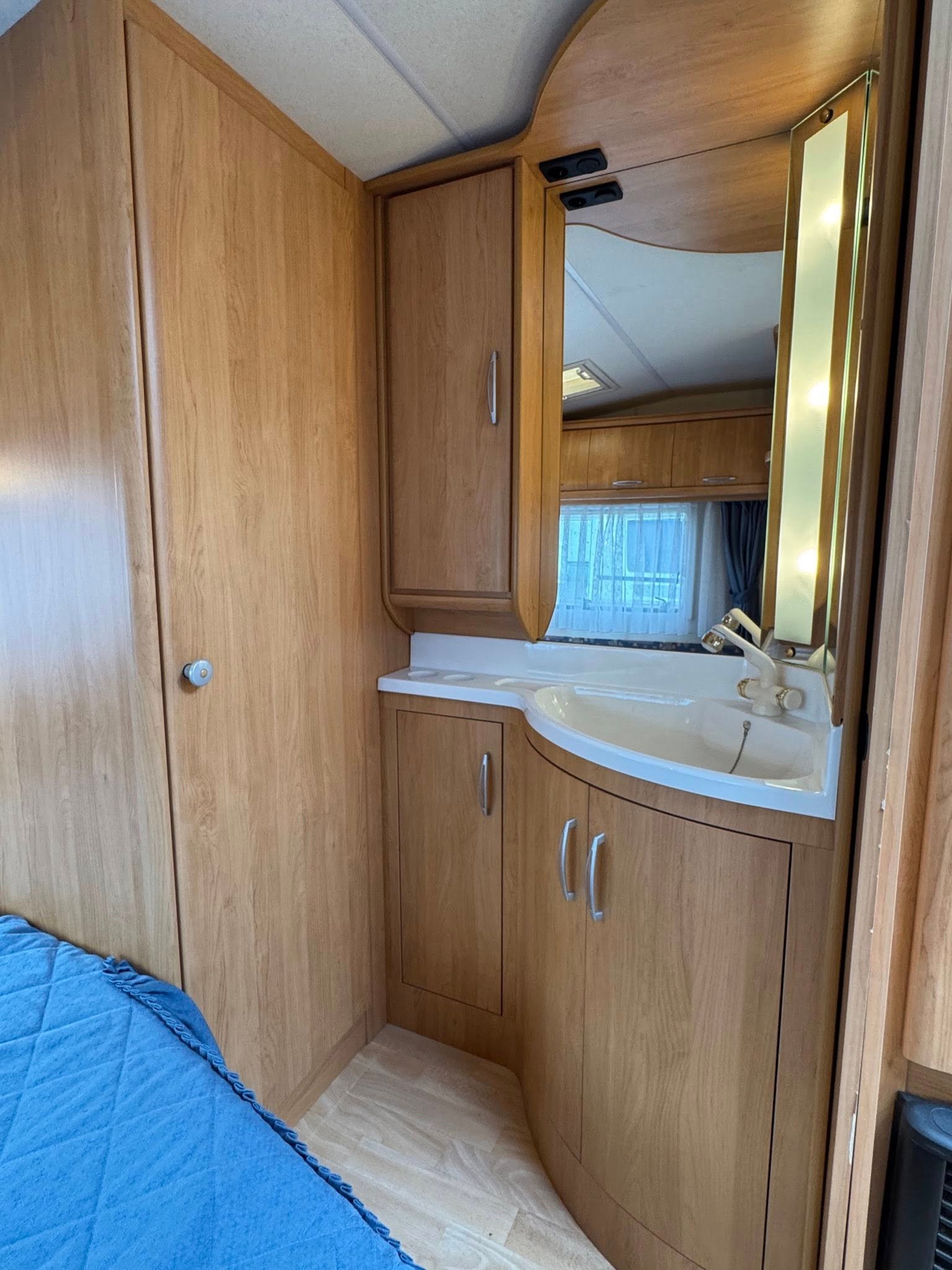 Interiér karavanu s dřevěnými skříňkami a umyvadlem. Příjemná atmosféra pro komfortní pobyt na cestách.