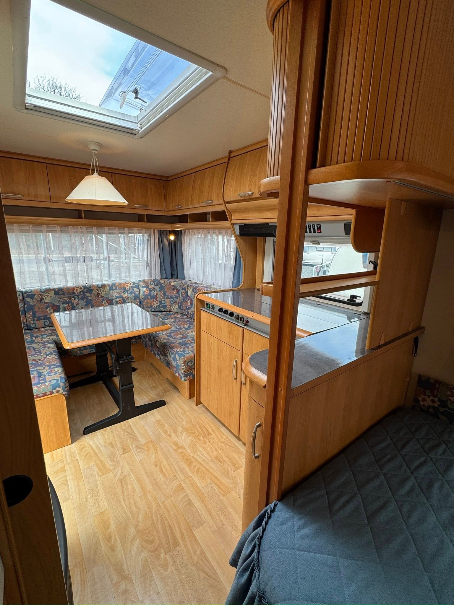 Stylový karavan s prostorným interiérem, dřevěnými prvky a pohodlným sezením pro relaxaci. Idealní pro výlety.