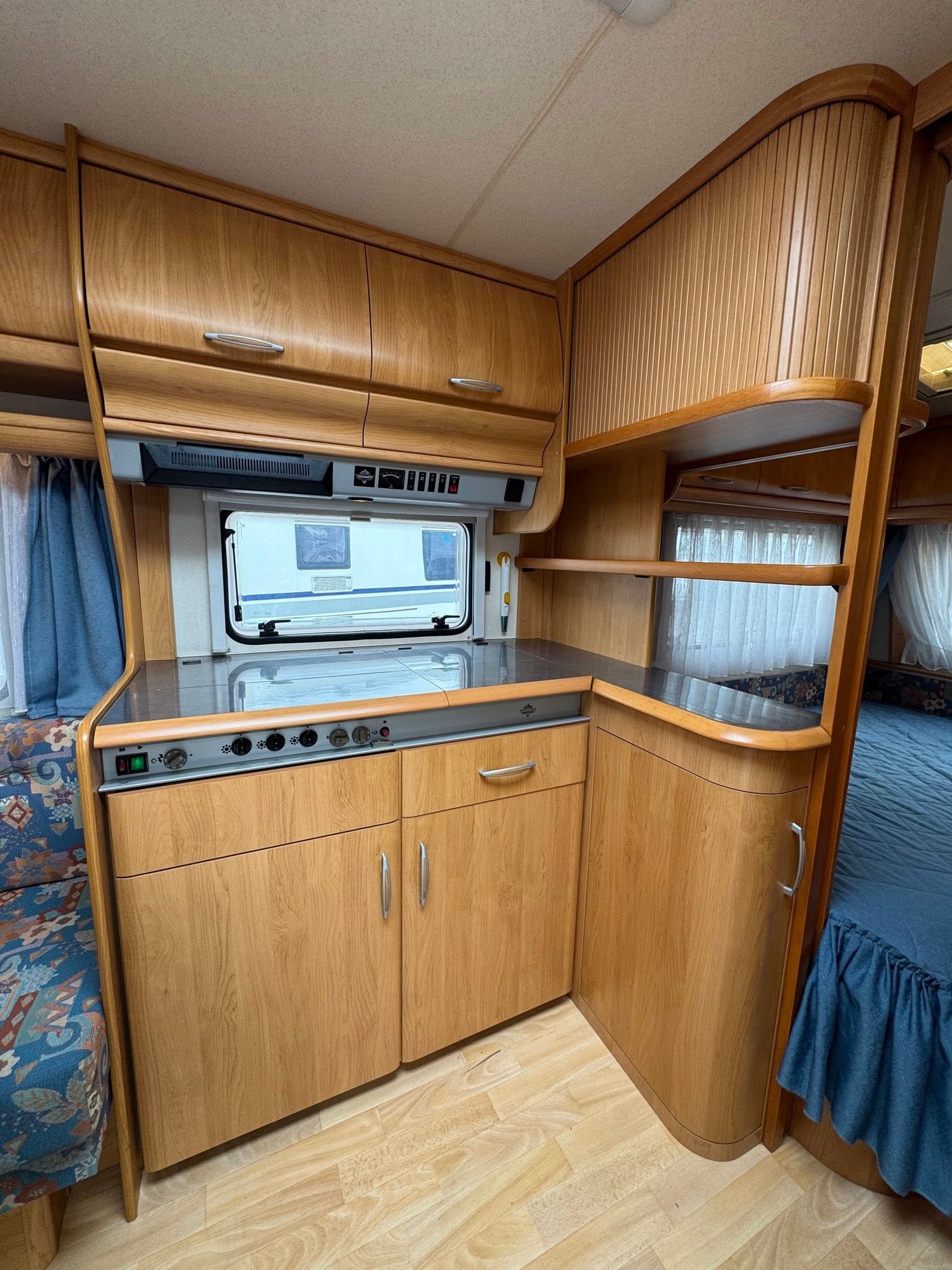 Interiér karavanu s dřevěnými skříněmi a kuchyňským koutem. Vhodné pro pohodlné cestování.