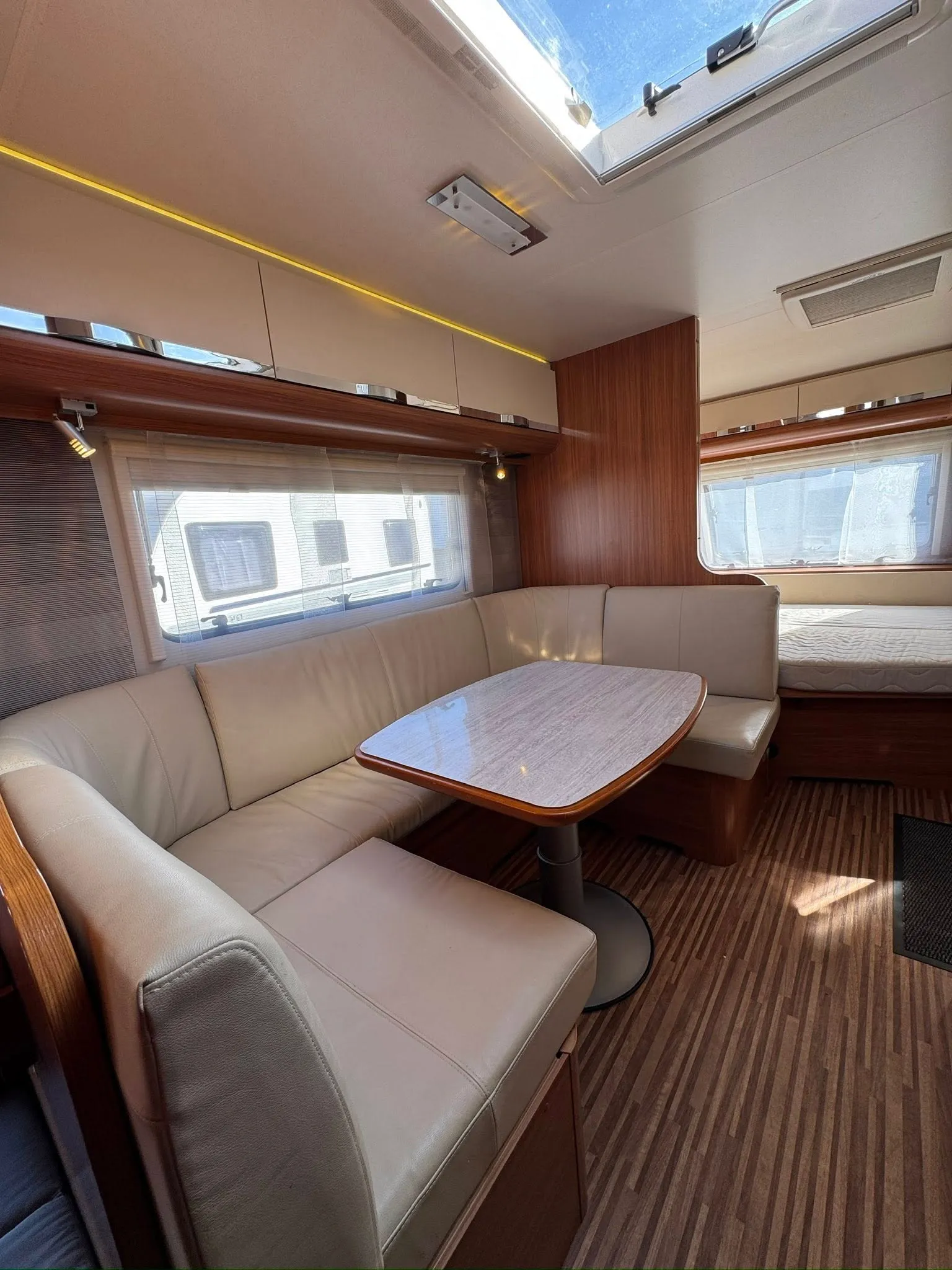 Interiér karavanu s pohodlným posezením a jídelním stolem. Vzdušný prostor a příjemné osvětlení.