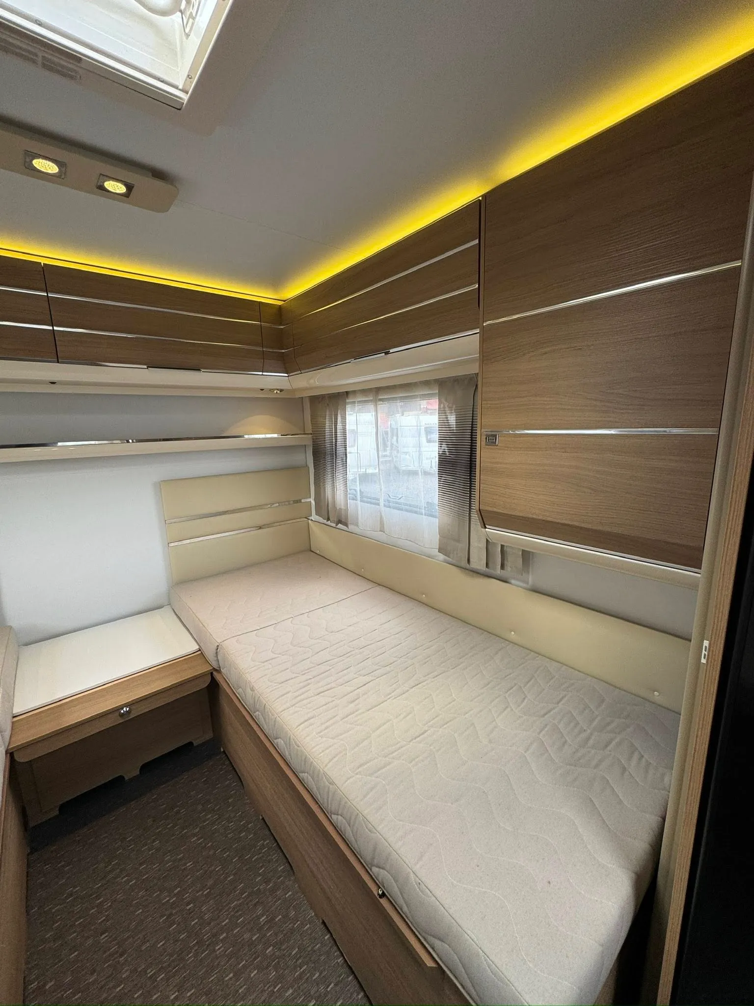 Obrázek ukazuje interiér karavanu s moderními dřevěnými prvky a pohodlným spací prostorem.