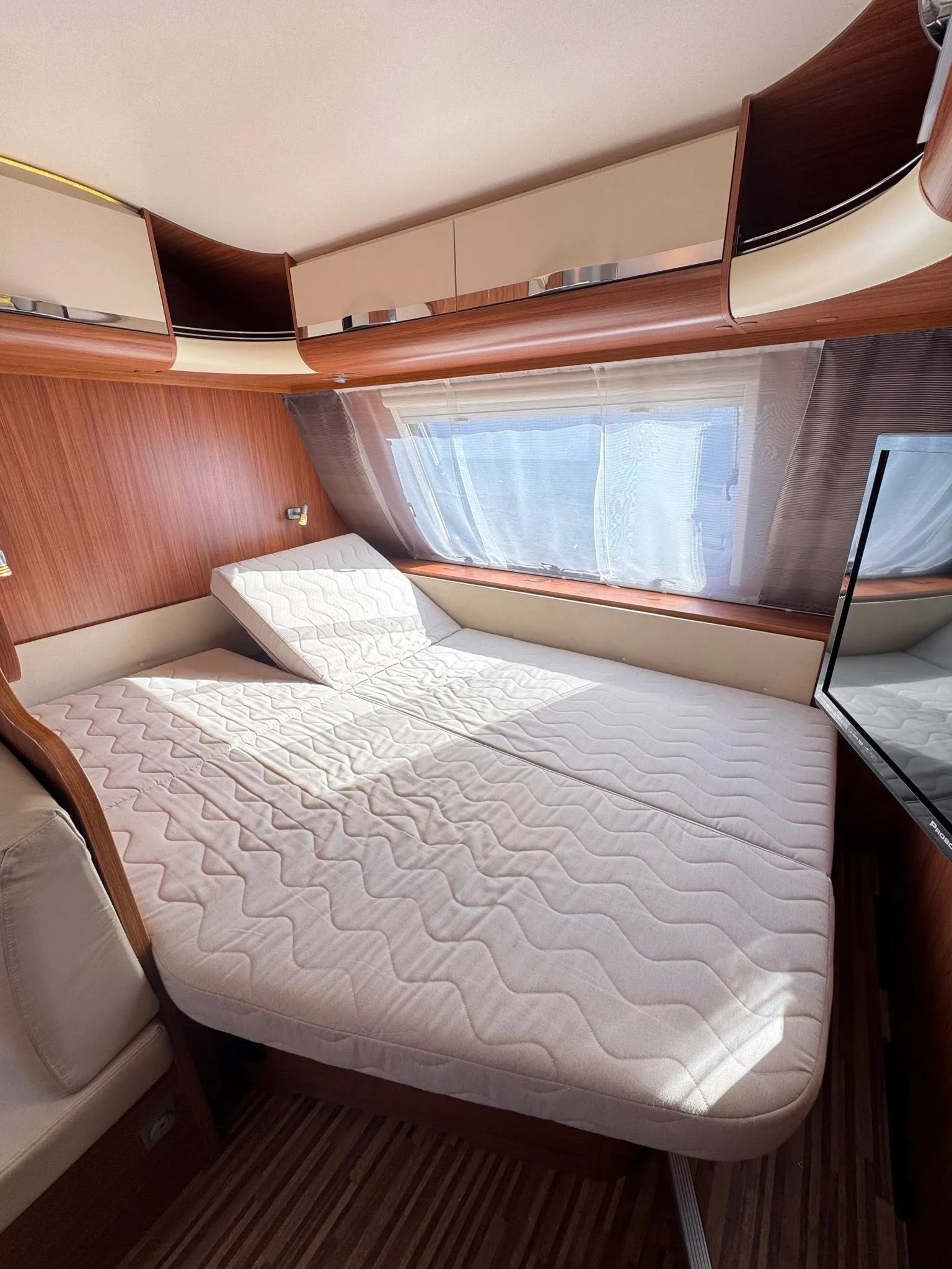 Obrázek ukazuje interiér karavanu s pohodlnou postelí a moderním zpracováním. Ideální pro cestování!