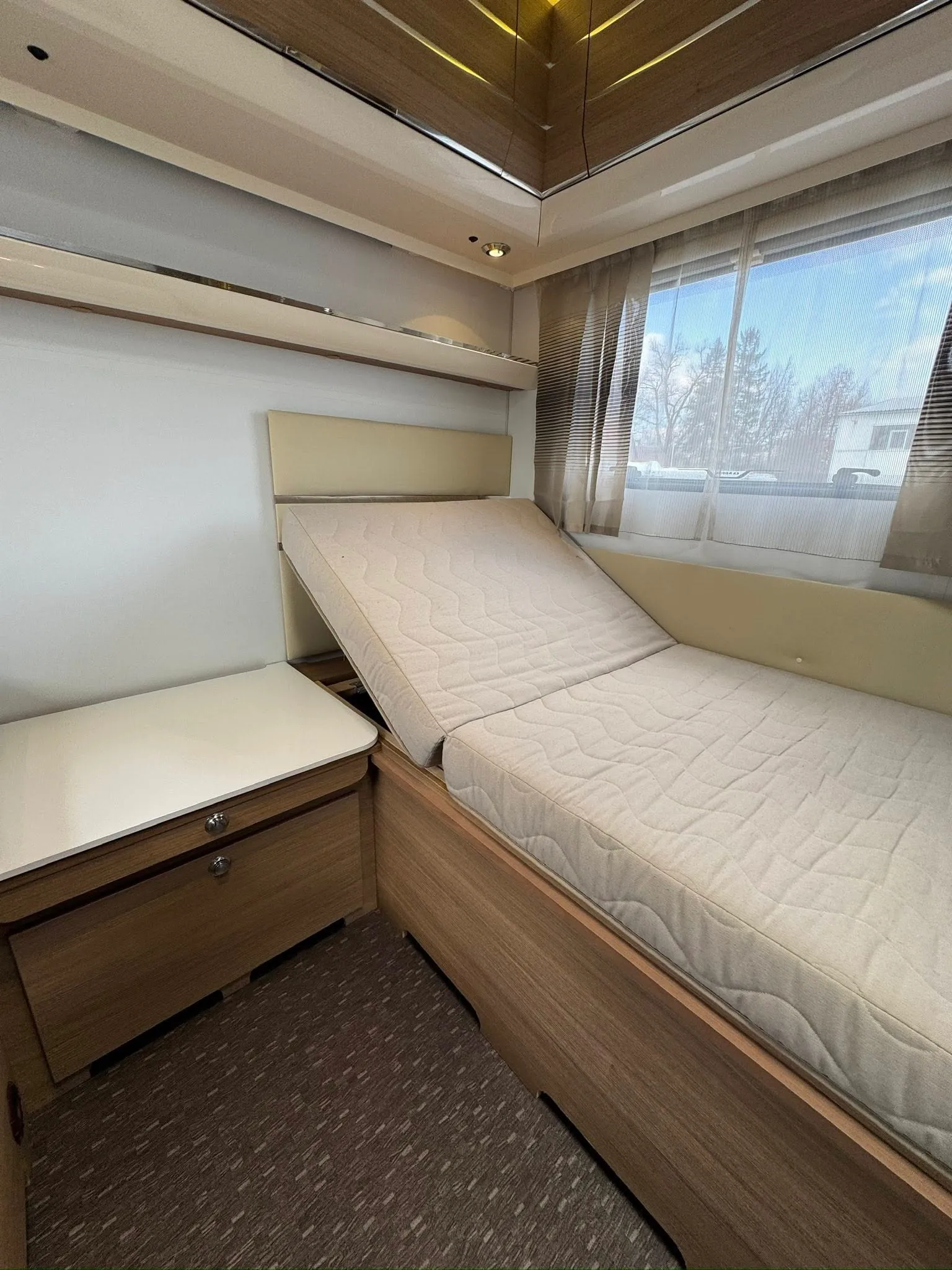 Obrázek interiéru obytného vozu s rozkládací postelí a úložným prostorem. Ideální pro pohodlné cestování.