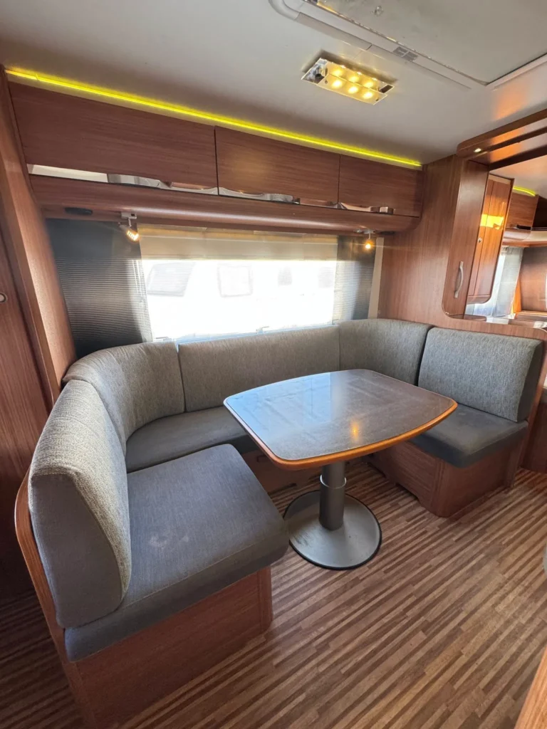 Obrázek interiéru karavanu s pohodlným sezením a stolečkem pro příjemné chvíle. Moderní design a funkčnost.