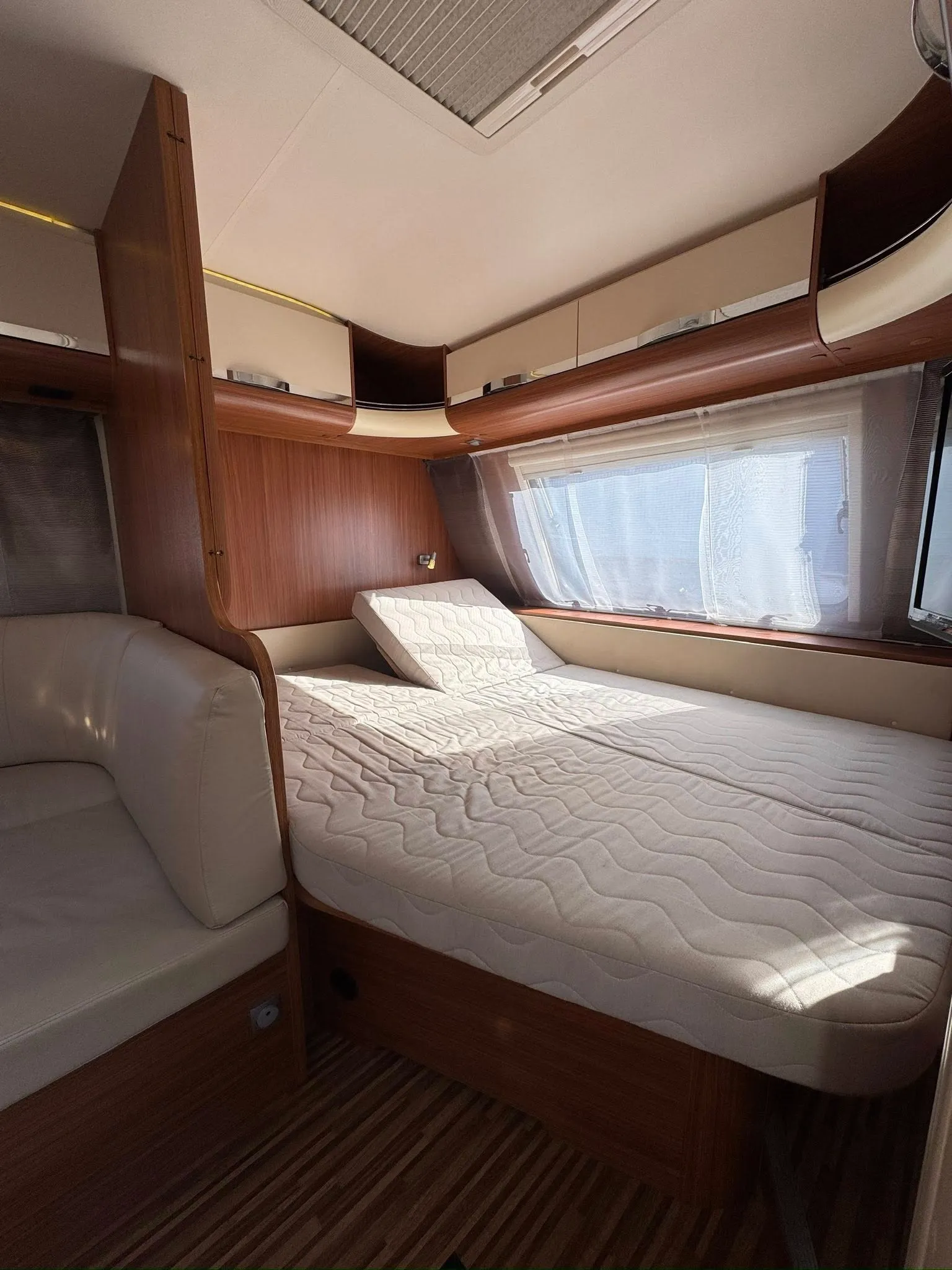 Interiér karavanu s manželskou postelí a pohodlným sezením. Moderní styl a příjemné světlo.