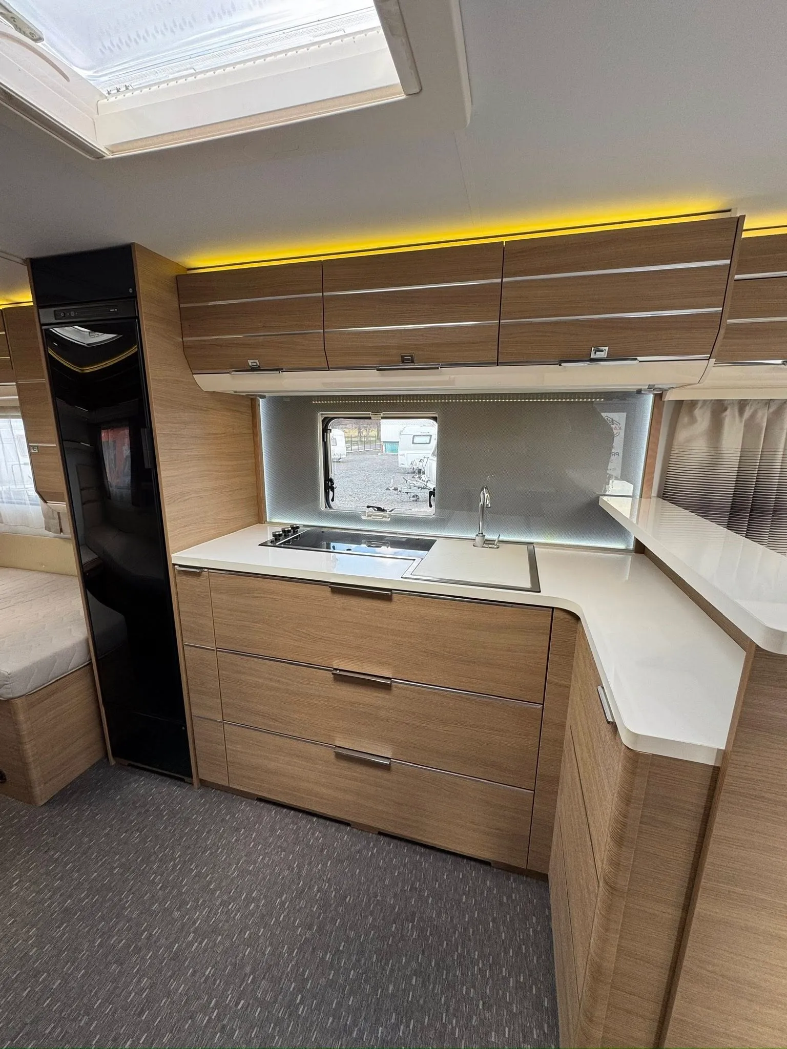 Obrázek interiéru karavanu s moderní kuchyňskou linkou a prostorným úložným prostorem.