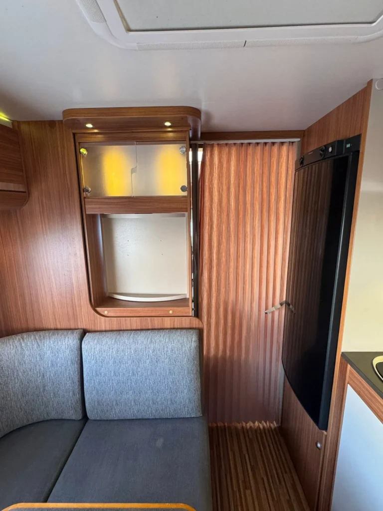 Obrázek interiéru karavanu s dřevěným designem, kuchyňskou linkou a útulným posezením.