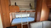 Obrázek interiéru karavanu s dřevěnými doplňky a výsuvným lůžkem. Ideální pro pohodlné cestování.