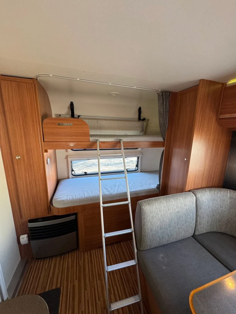 Obrázek interiéru karavanu s dřevěnými doplňky a výsuvným lůžkem. Ideální pro pohodlné cestování.