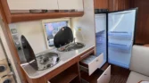 Interiér obytného auta, moderní kuchyňka, lednice a úložné prostory. Ideální pro cestování a kempování.