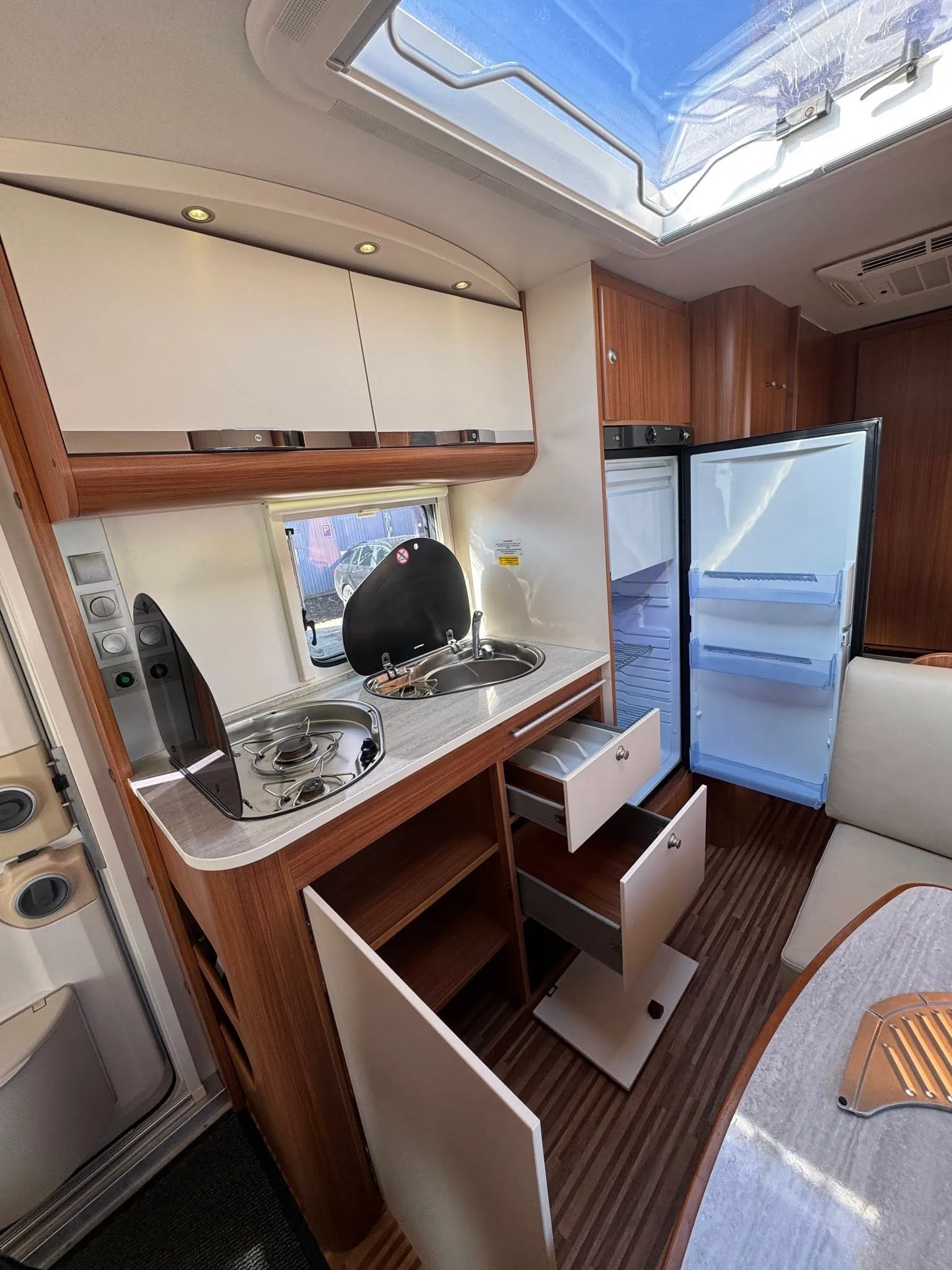 Interiér obytného auta, moderní kuchyňka, lednice a úložné prostory. Ideální pro cestování a kempování.