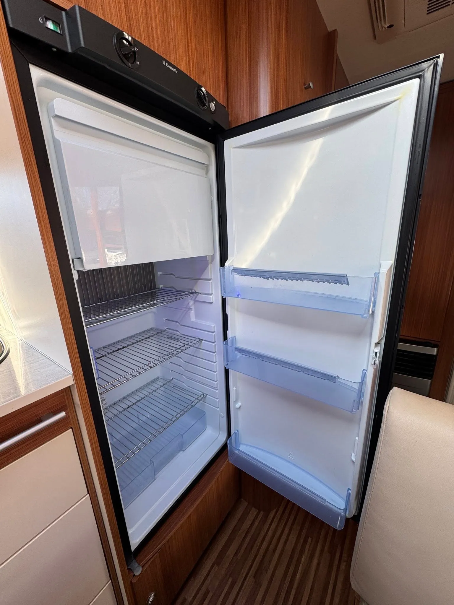 Obrázek zobrazuje interiér obytného vozu s moderní lednicí značky Dometic. Ideální pro kempování a cestování.