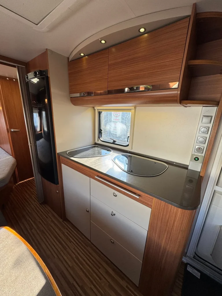 Obrázek interiéru karavanu s moderní kuchyní a úložnými prostory. Komfortní a stylový design pro cestování.