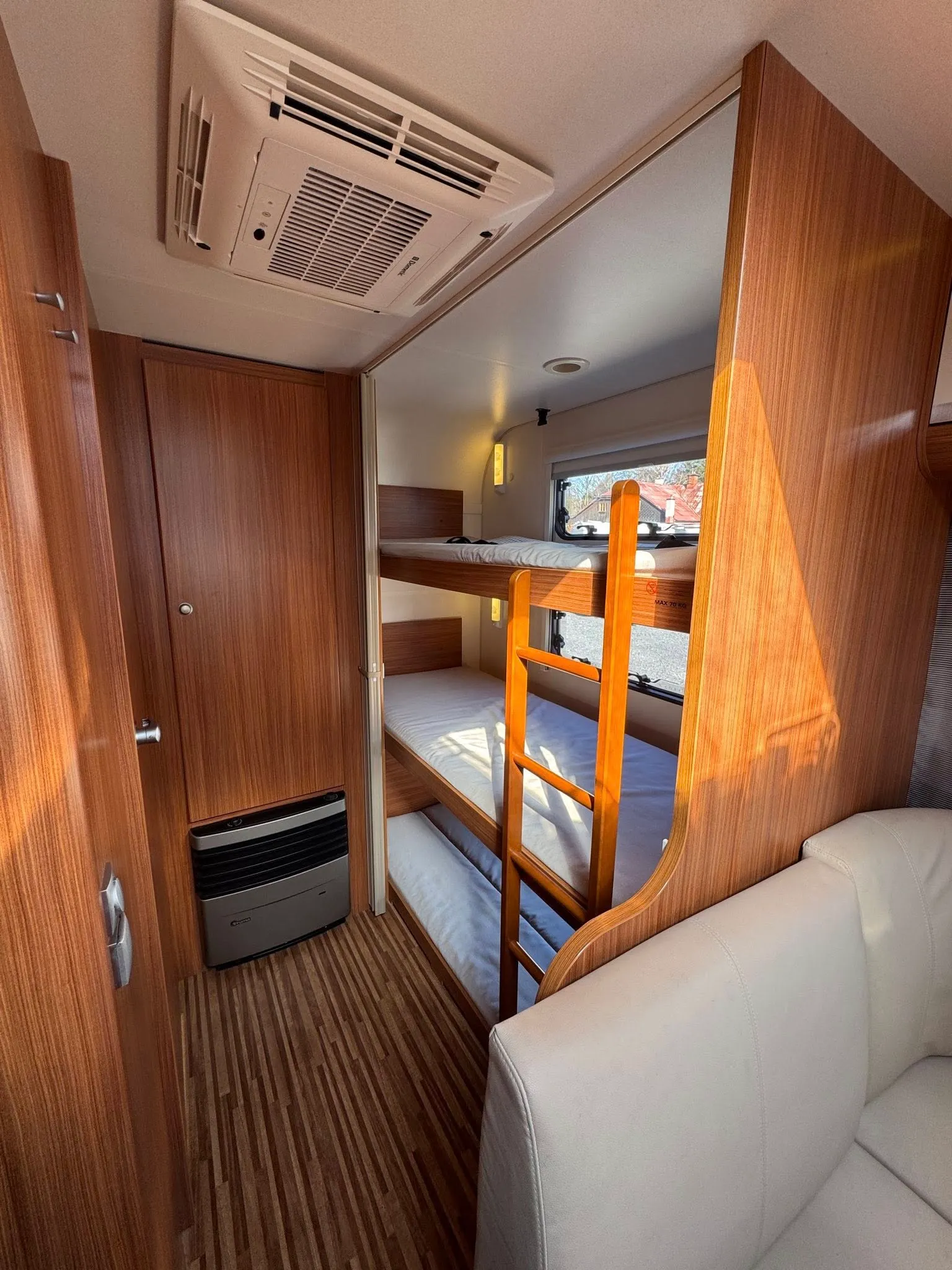 Obrázek interiéru obytného auta s dřevěným obložením a patrovou postelí. Prostorný a útulný design.