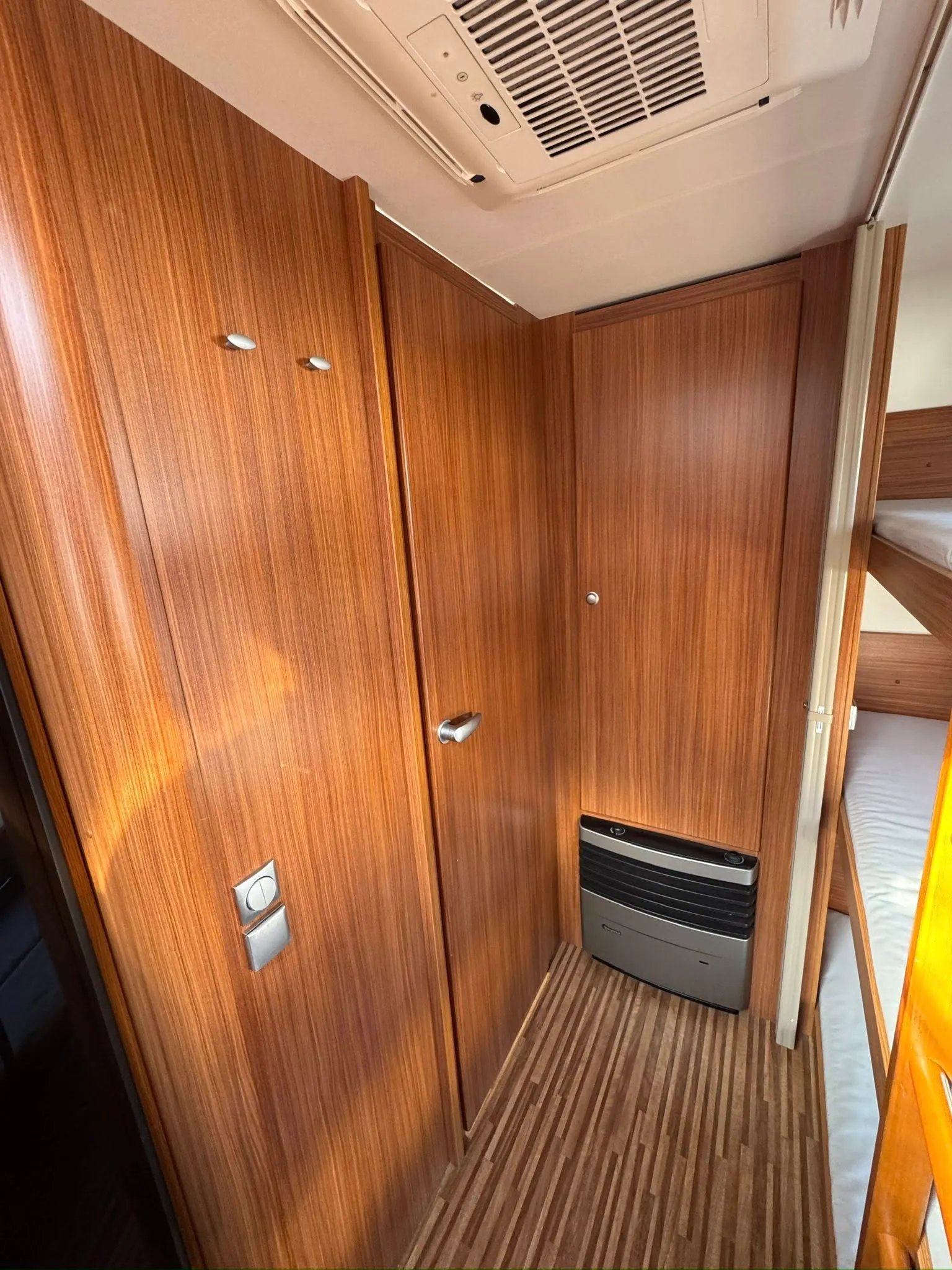 Obrázek interiéru obytného auta s dřevěnými panely a úložnými prostory. Značka a model nejsou viditelné.