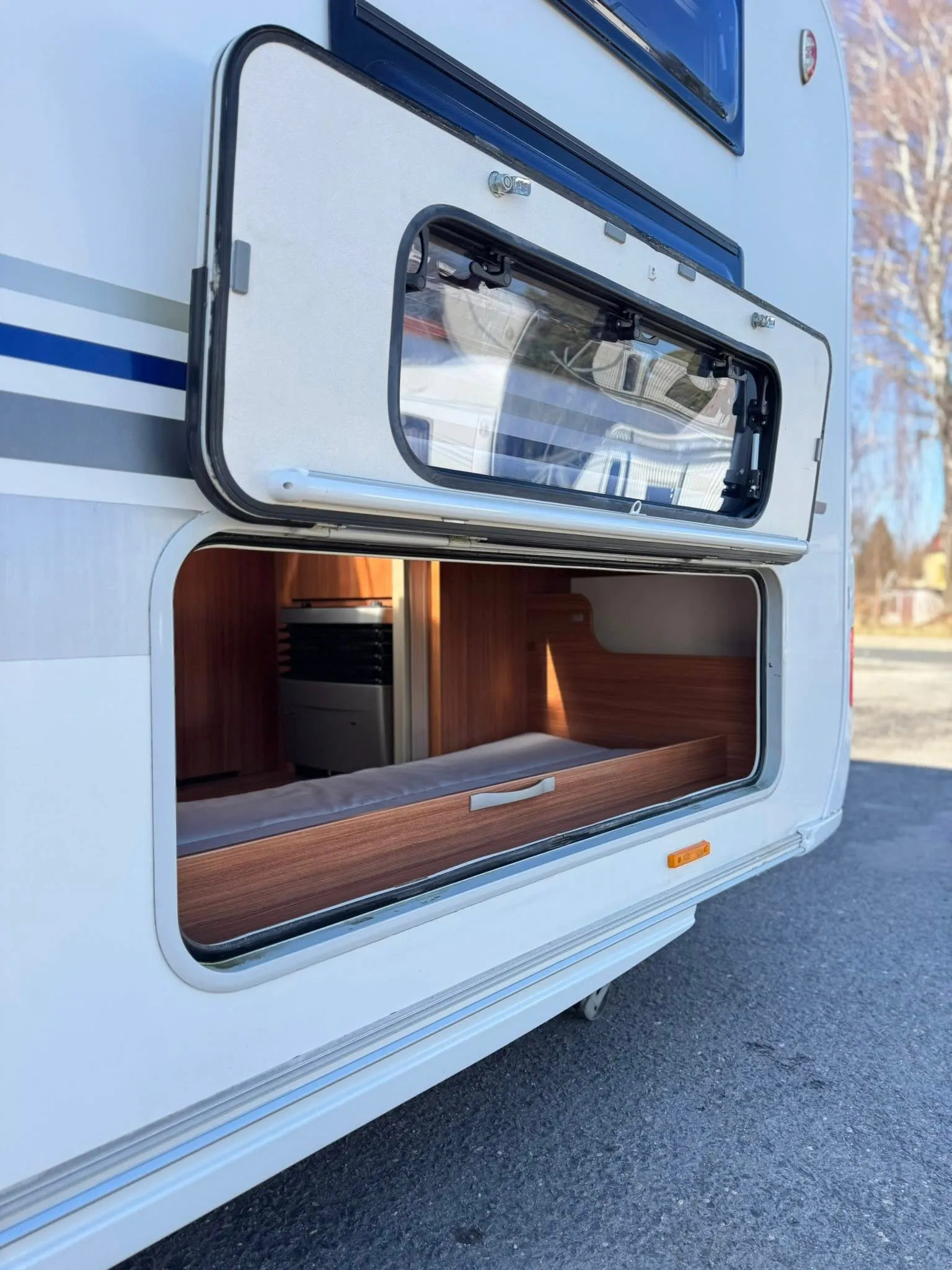 Obrázek ukazuje úložný prostor obytného auta s dřevěným nábytkem. Značka a model nejsou specifikovány.