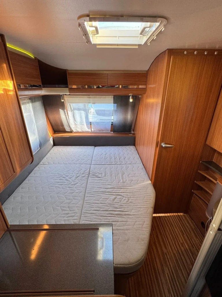 Obrázek interiéru karavanu s dřevěným obložením a pohodlnou ložnou plochou. Ideální pro rodinné výlety.