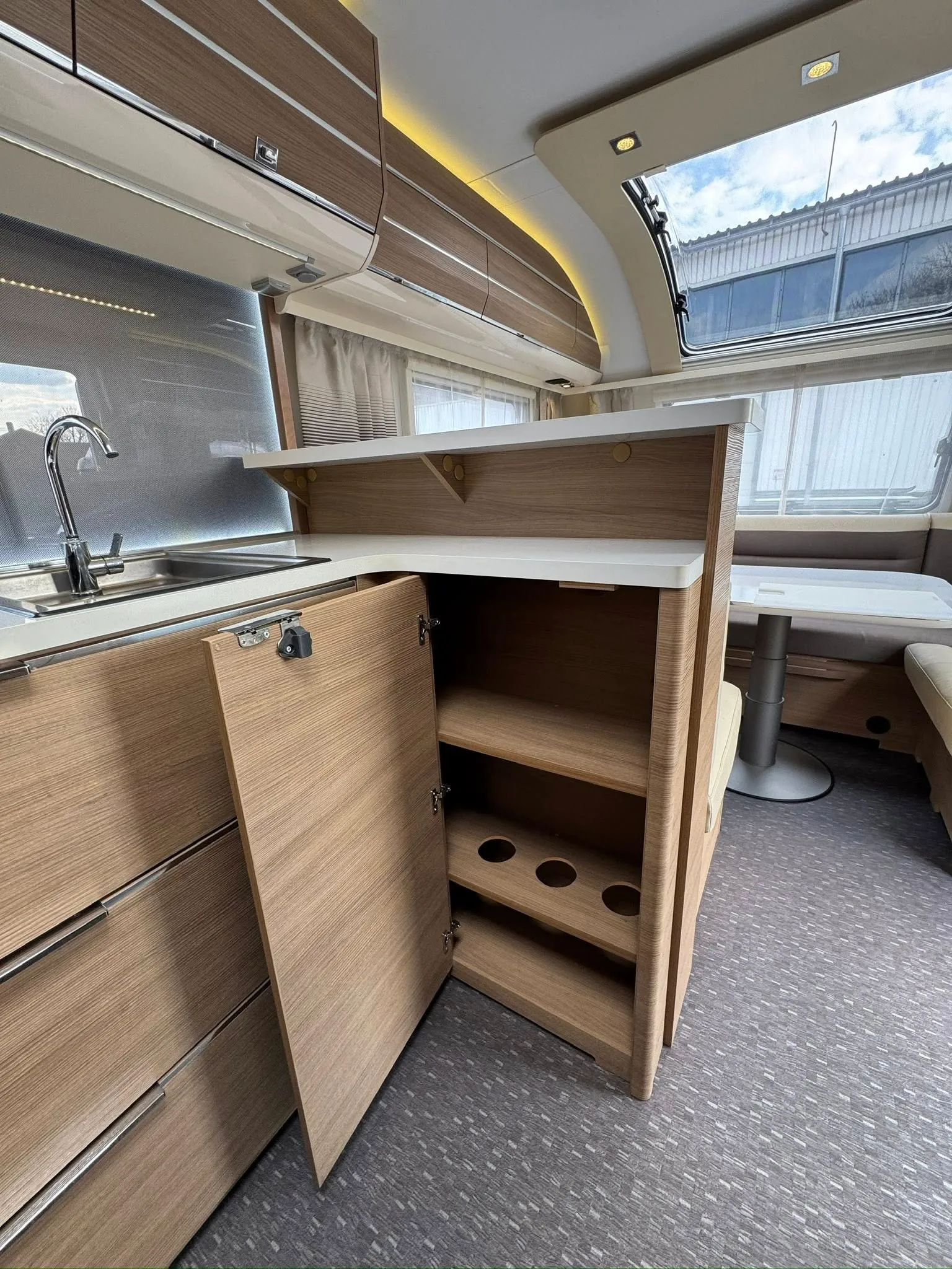 Obrázek interiéru moderního karavanu s dřevěnými skříňkami a kuchyňským koutem. Elegantní a prostorné uspořádání.