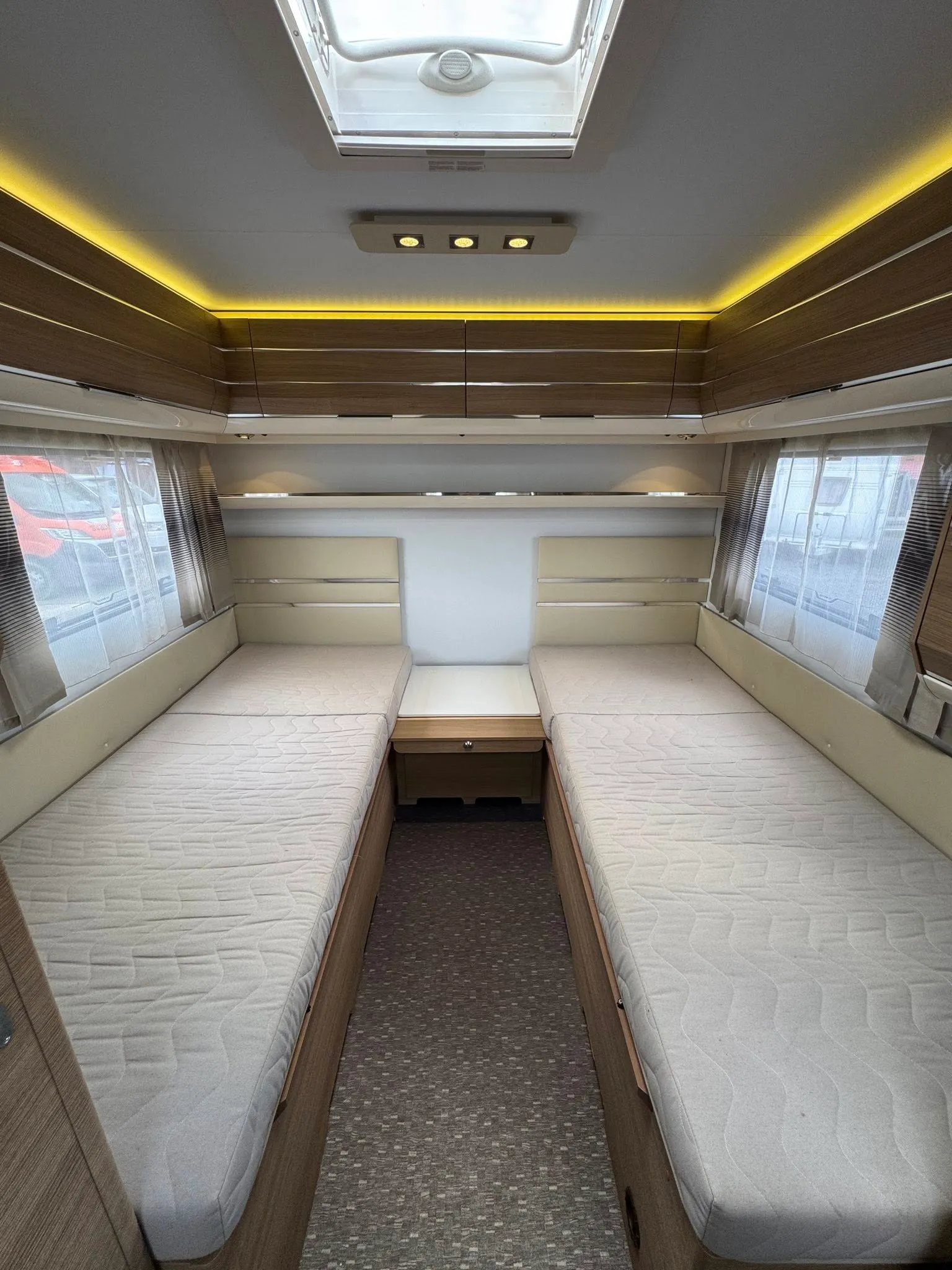 Obrázek interiéru karavanu s dvoumi lůžky a moderním osvětlením. Ideální pro komfortní cestování.