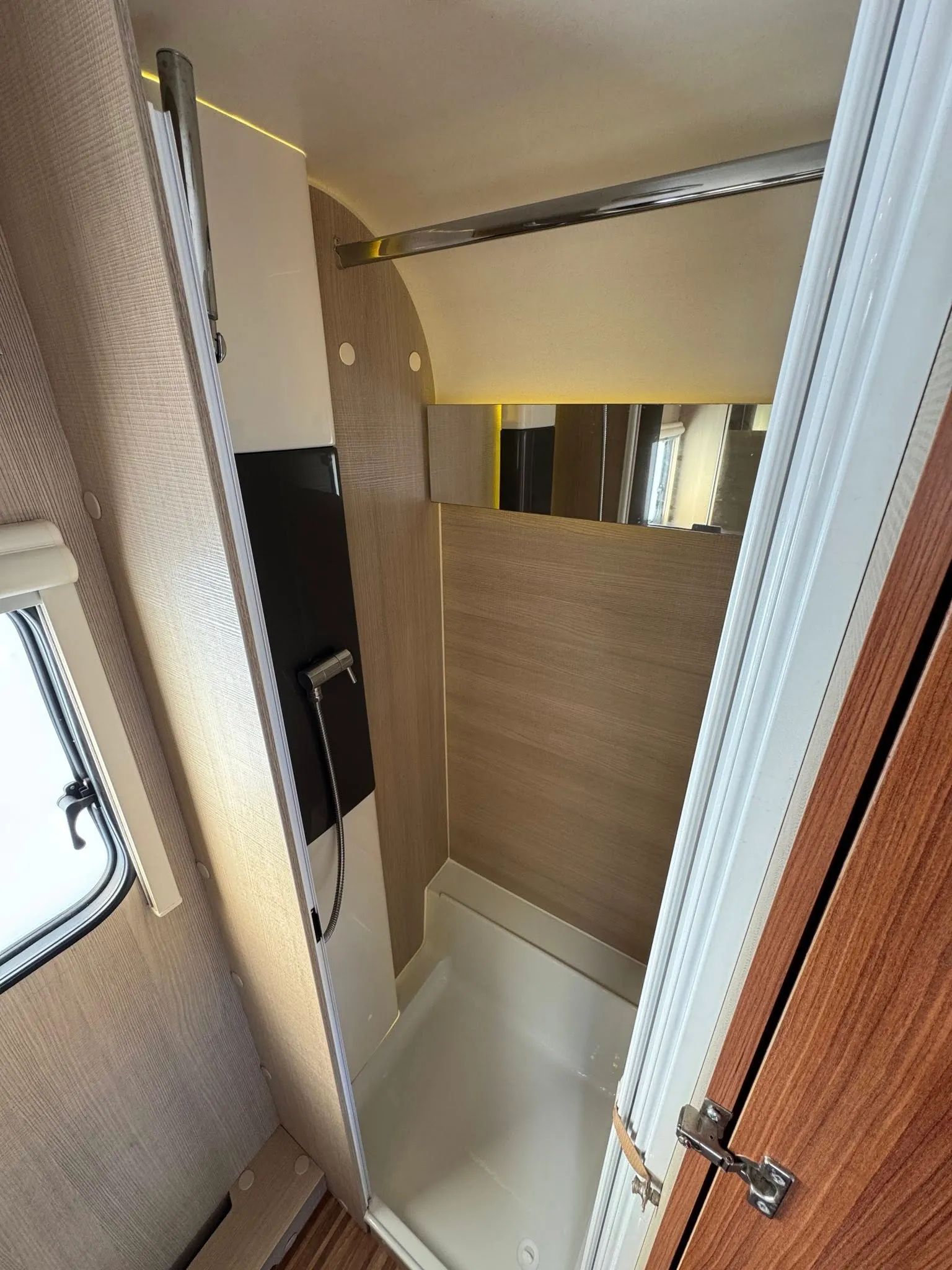 Obrázek ukazuje moderní koupelnu v karavanu. Uvnitř je sprchový kout a elegantní design interiéru.