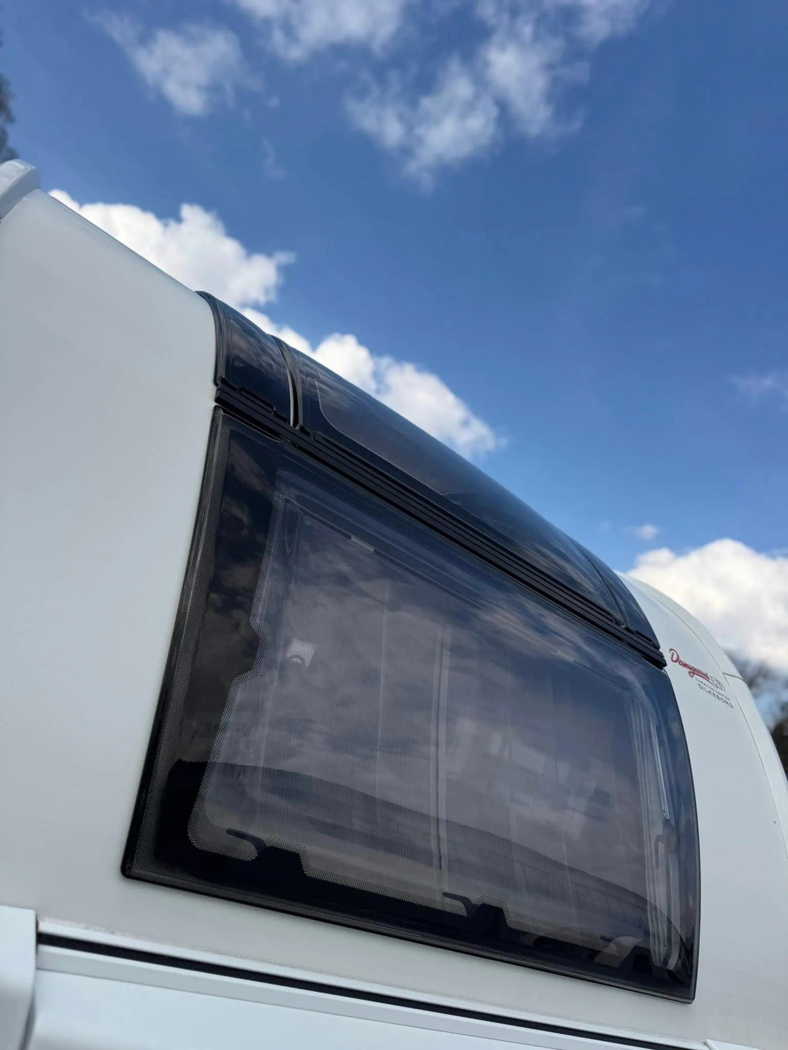 Na obrázku je karavan s moderním designem a velkým oknem, ideální pro dobrodružství v přírodě.