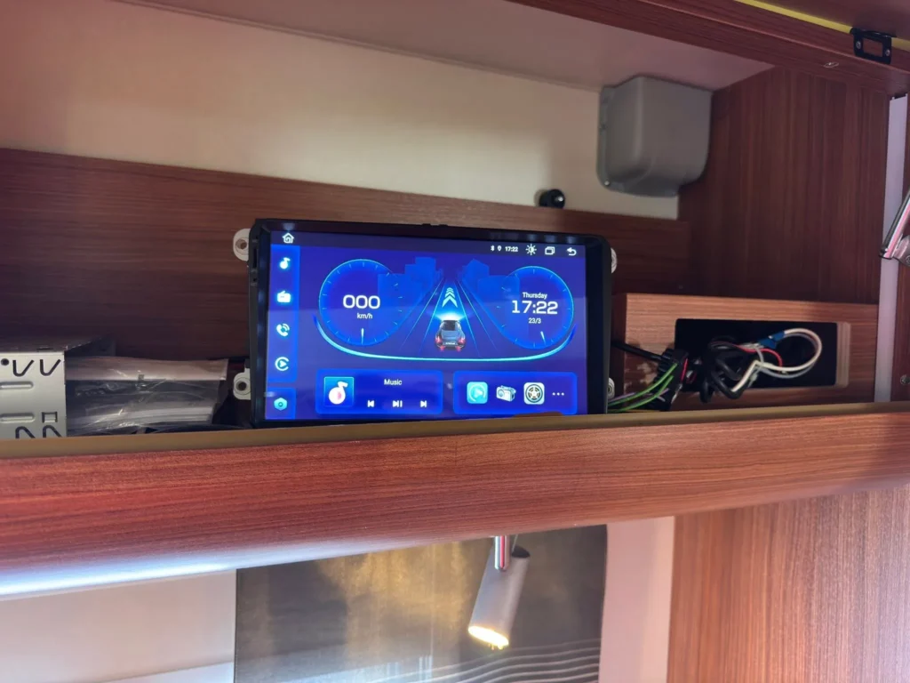 Obrázek ukazuje moderní palubní systém v obytném autě, s digitálním displejem a připojením pro hudbu.