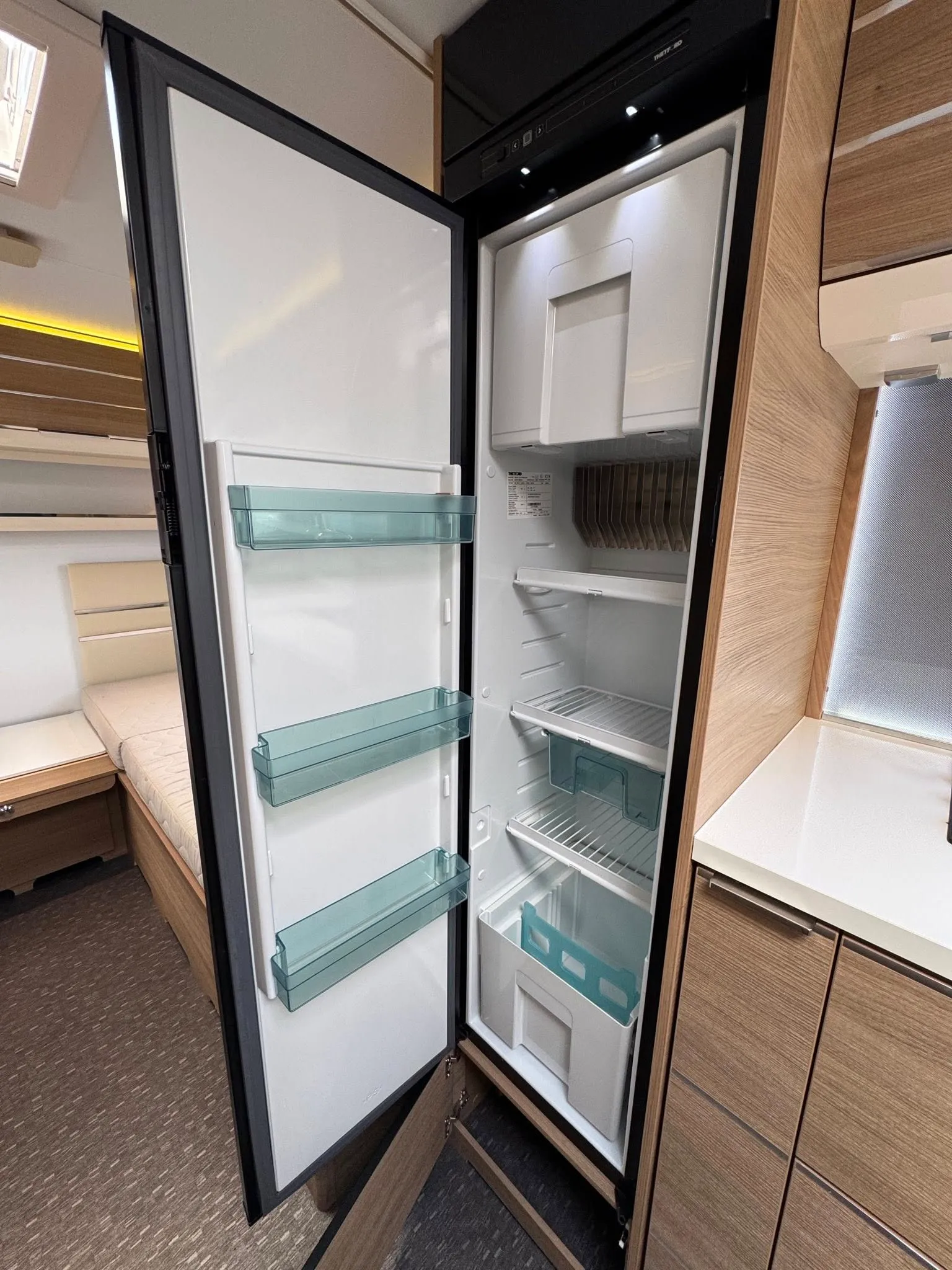 Obrázek zobrazuje interiér karavanu s velkým lednicí. Moderní design a funkční uspořádání pro komfortní cestování.