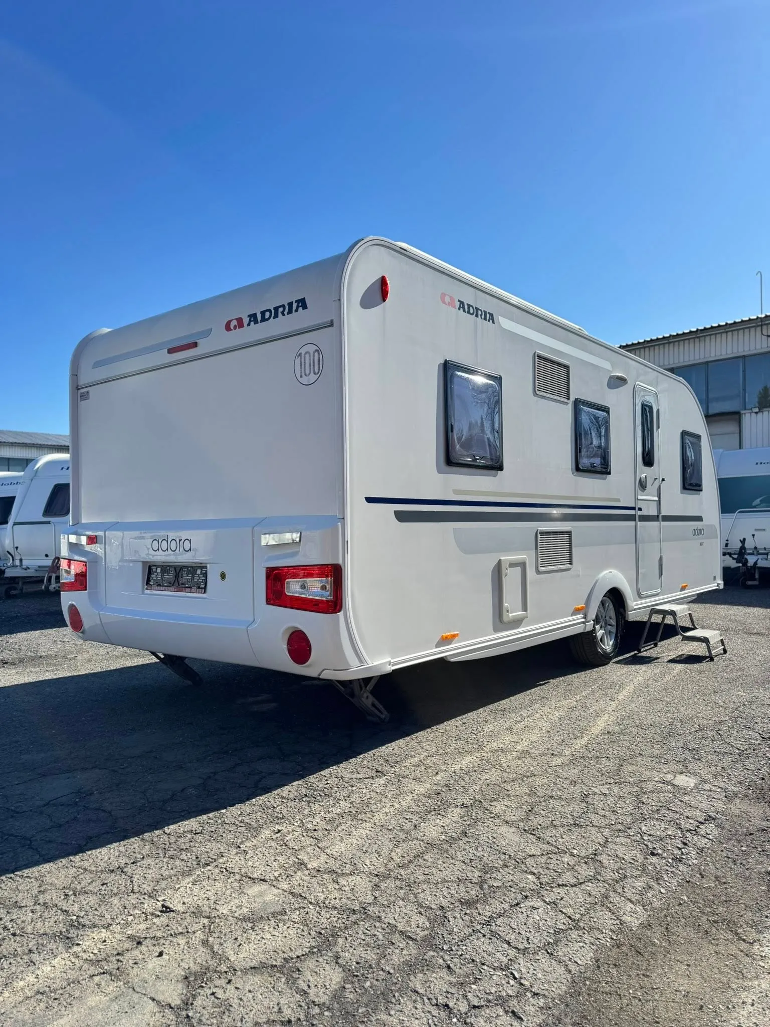 Karavan Adria Adora na slunném parkovišti, s elegantním designem a prostorným interiérem. Ideální pro dobrodružství!