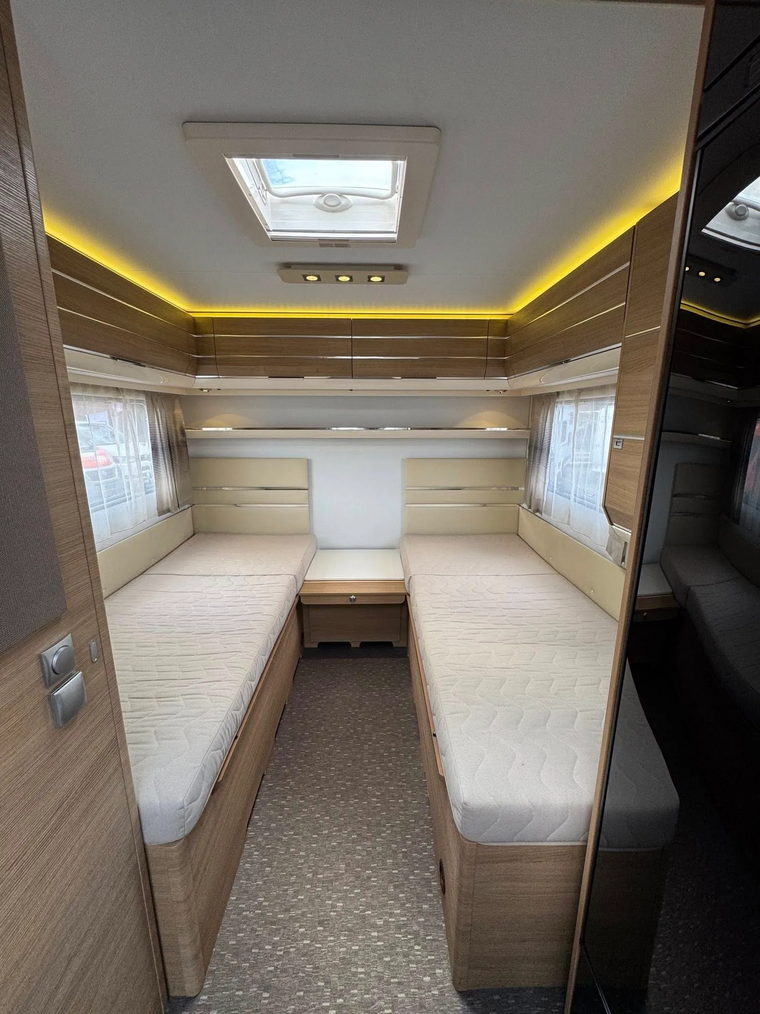 Interiér karavanu s dvěma lůžky a moderním designem, ideální pro pohodlné cestování.